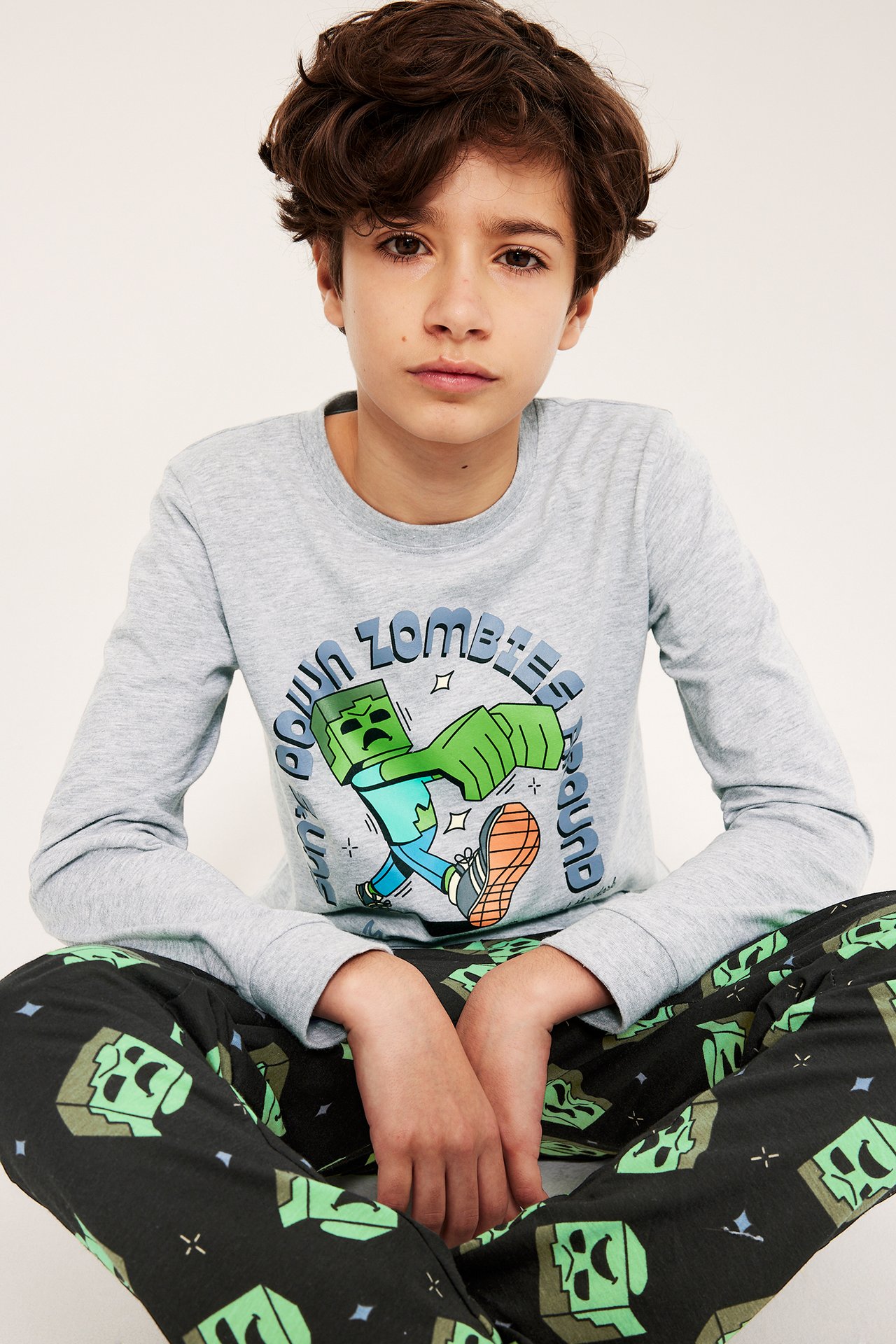 Edestä, lapsi vaaleanharmaassa pitkähihaisessa Minecraft-kuviollisessa pyjamapaidassa ja mustissa kuviohousuissa.