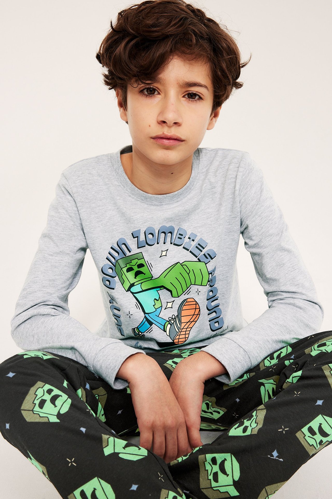 Edestä, lapsi vaaleanharmaassa pitkähihaisessa Minecraft-kuviollisessa pyjamapaidassa ja mustissa kuviohousuissa.