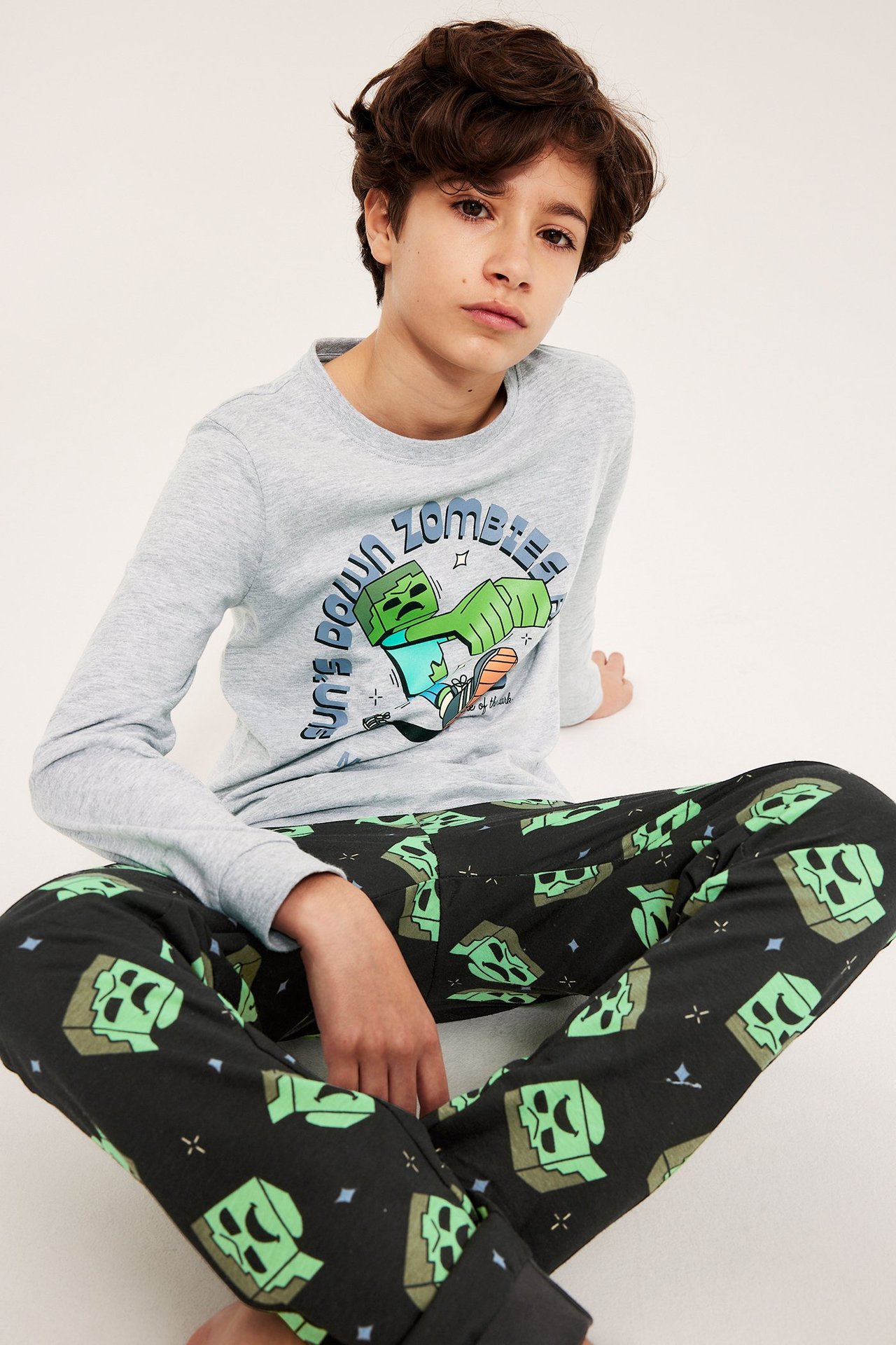 Edestä kuvattu lapsi yllään harmaa pitkähihainen Minecraft-pyjamatoppi ja mustat zombikuosiset housut.
