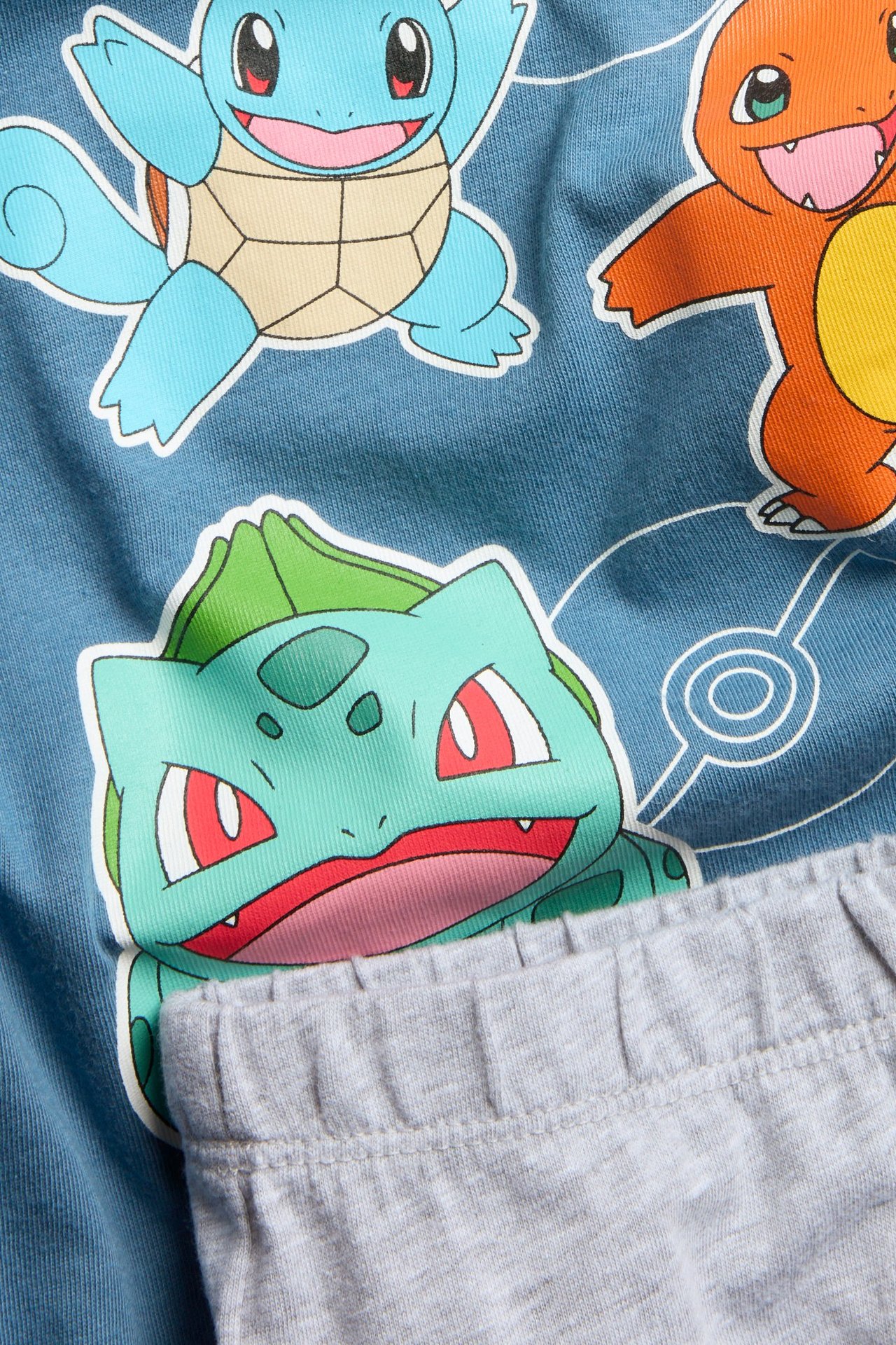 Lähikuva lasten sinisestä pyjamapaidasta, jossa on värikäs Pokémon-kuvio, ja harmaista pyjamahousuista.