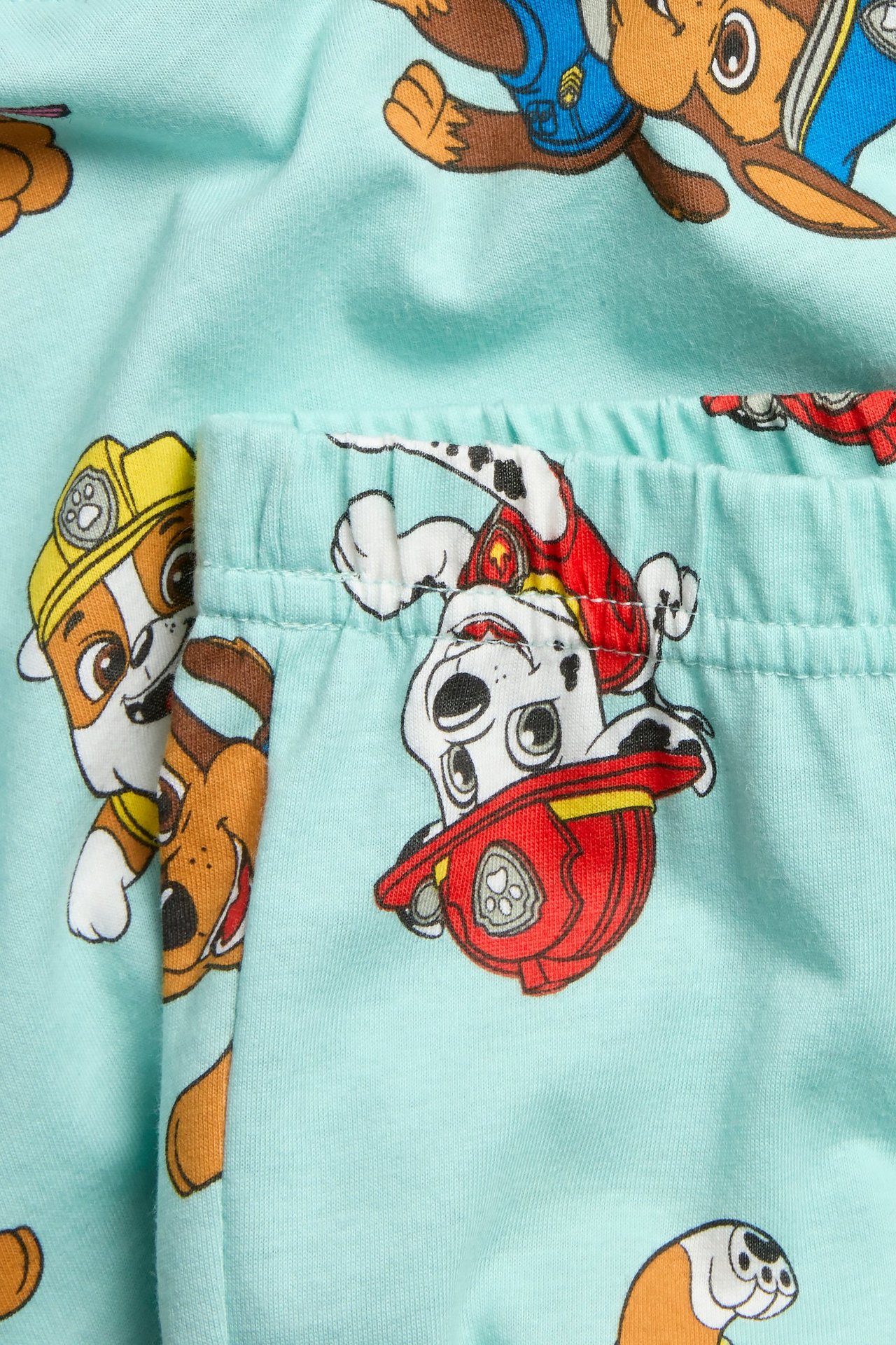 Lähikuva vaaleanturkoosista puuvillaisesta lasten pyjamasta, jossa on Ryhmä Hau -kuvio ja joustava vyötärö.