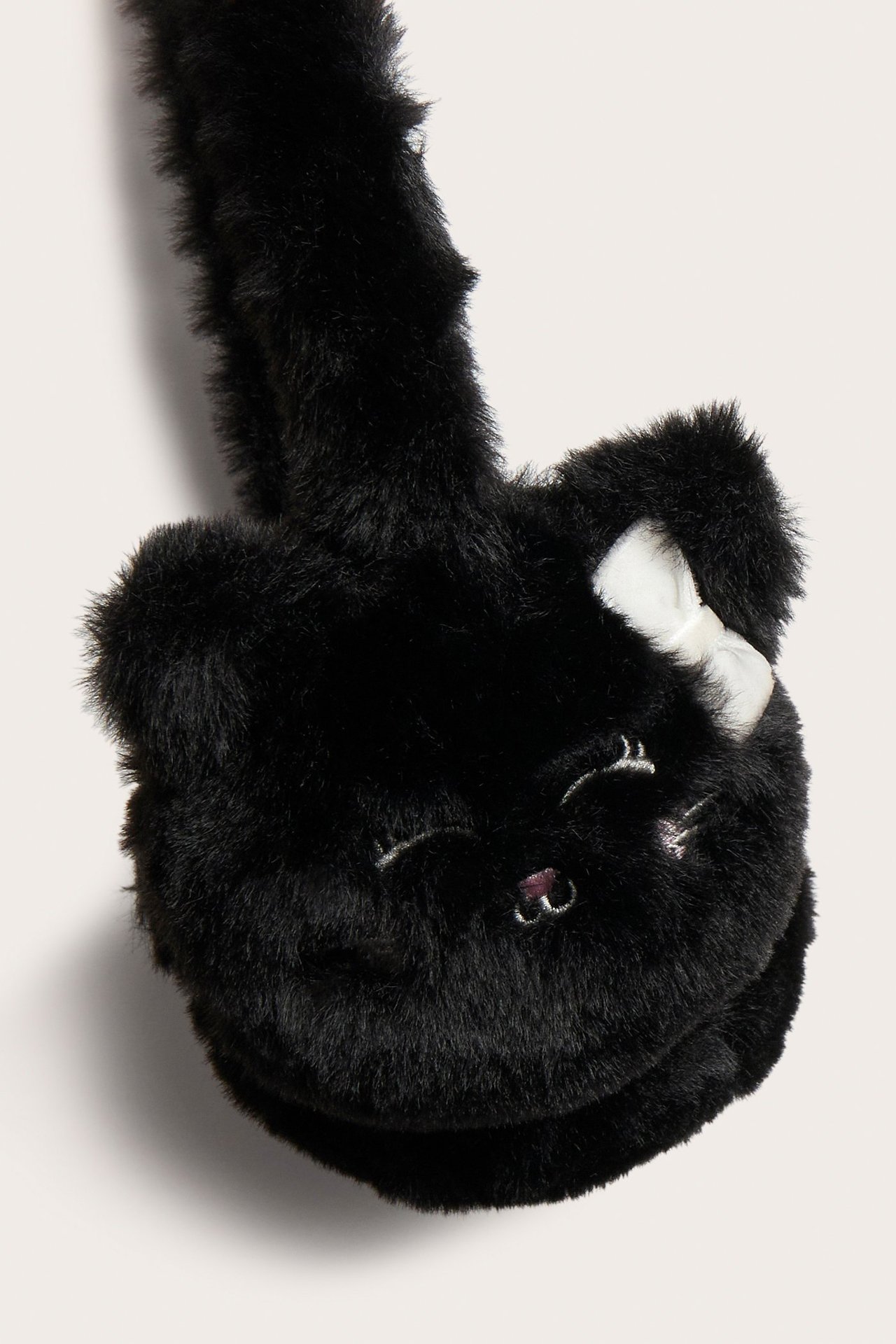 Zbliżenie na czarne puszyste nauszniki z motywem kota i białą kokardką na jednej słuchawce.