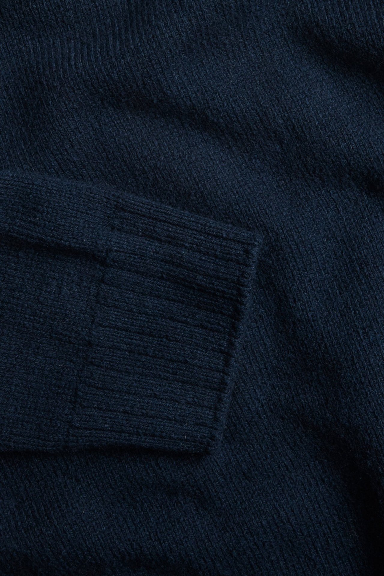 Zbliżenie na granatowy melanżowy dzianinowy golf, ukazujące prążkowany mankiet.