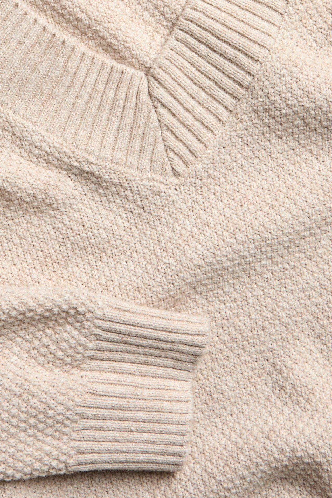 Zbliżenie na beżowy, melanżowy sweter męski z dekoltem w serek, z fakturą i ściągaczami.