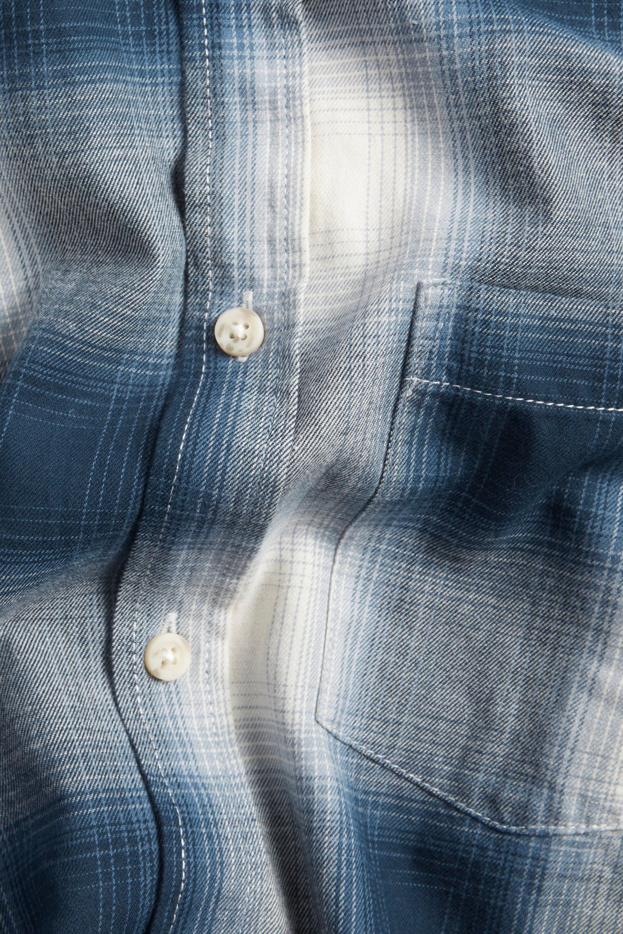 Zbliżenie męskiej koszuli flanelowej w ciemnoniebieską i białą kratę z białymi guzikami i kieszenią na piersi.