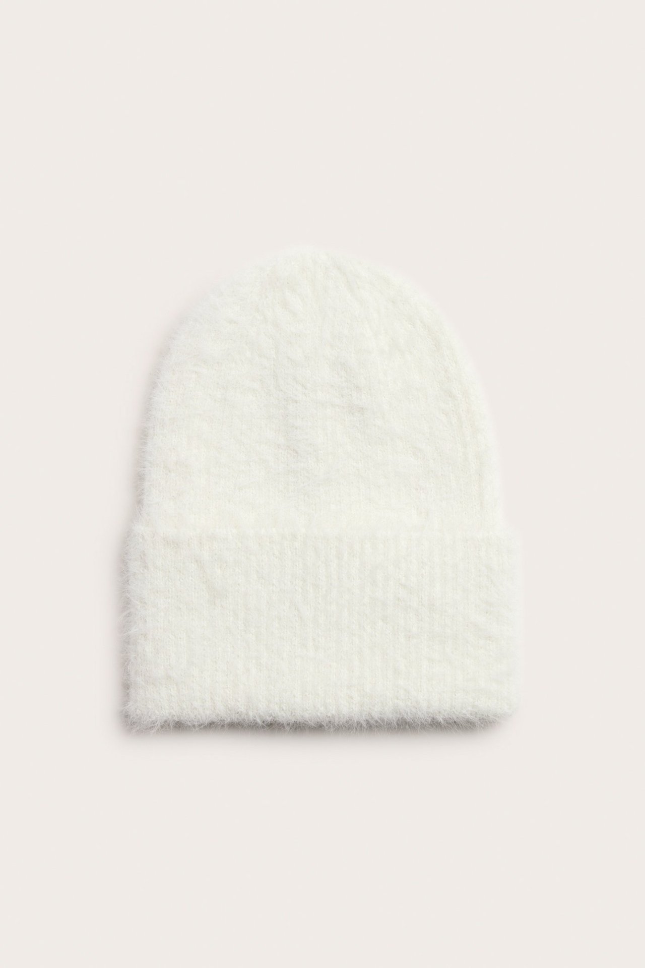 Widok z przodu na miękką, kremową czapkę beanie z poliestru z podwiniętym brzegiem.