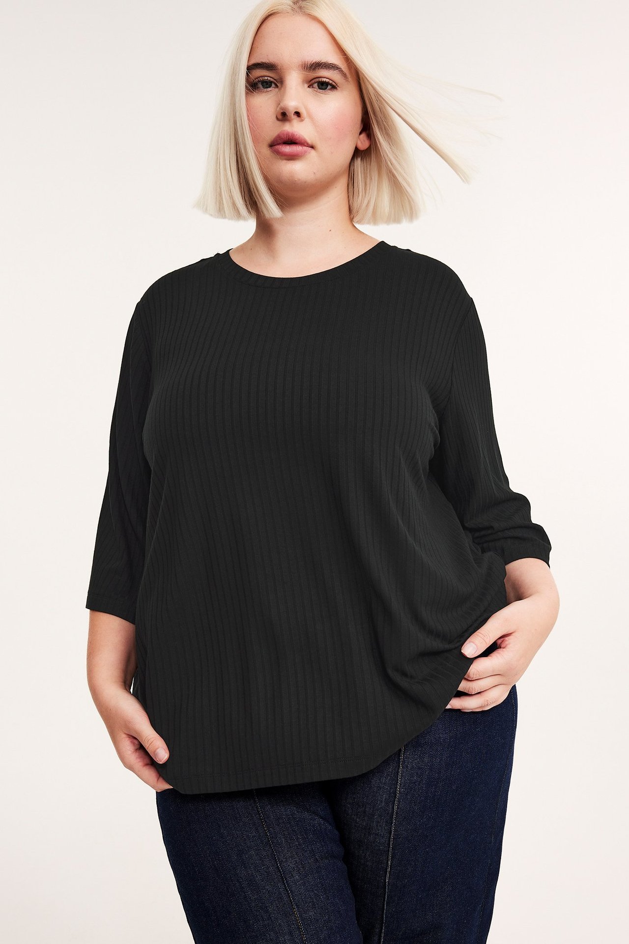 Edestä näkymä naisesta, yllään musta ribattu viskoositoppi 3/4-hihoilla ja tummansiniset farkut.