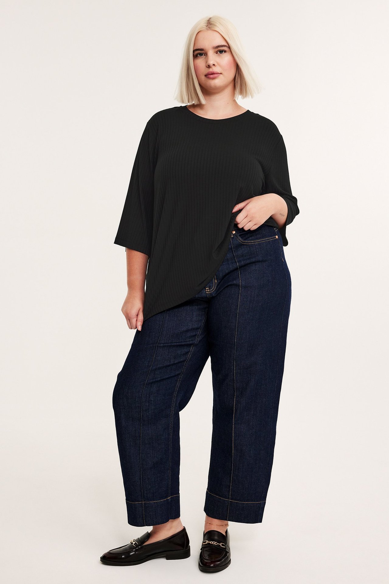Widok z przodu: kobieta w czarnym prążkowanym topie wiskozowym 3/4 rękawem, ciemnoniebieskich jeansach, brązowych mokasynach.