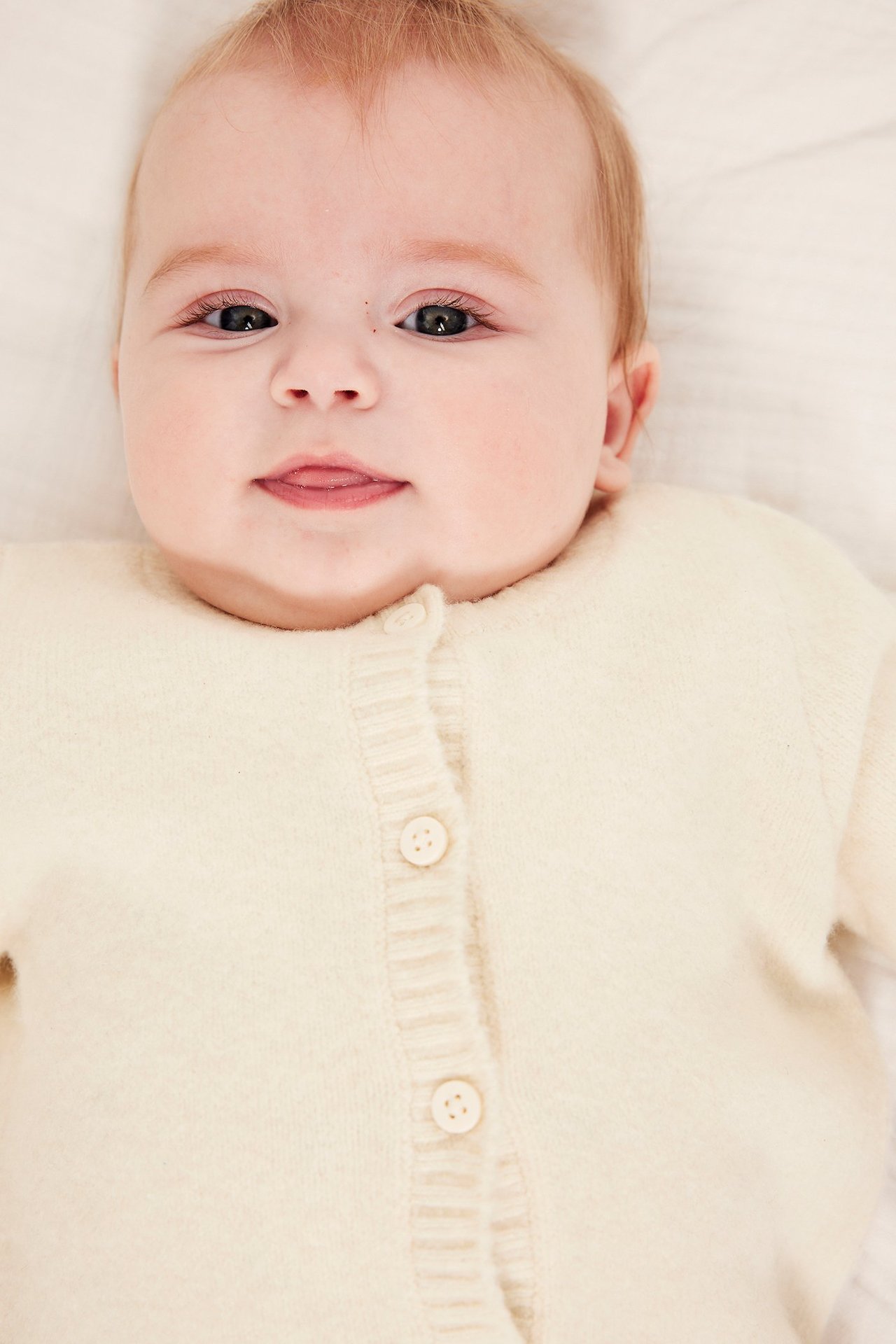 Närbild framifrån på en baby i en ljusbeige stickad kofta med knappar fram.