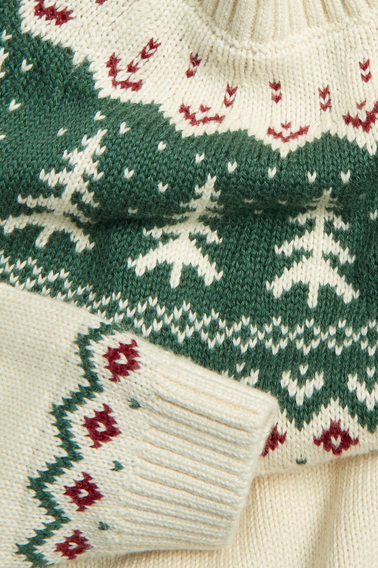 Nærbilde av en offwhite strikket julegenser med grønt og rødt jacquard-granmønster.