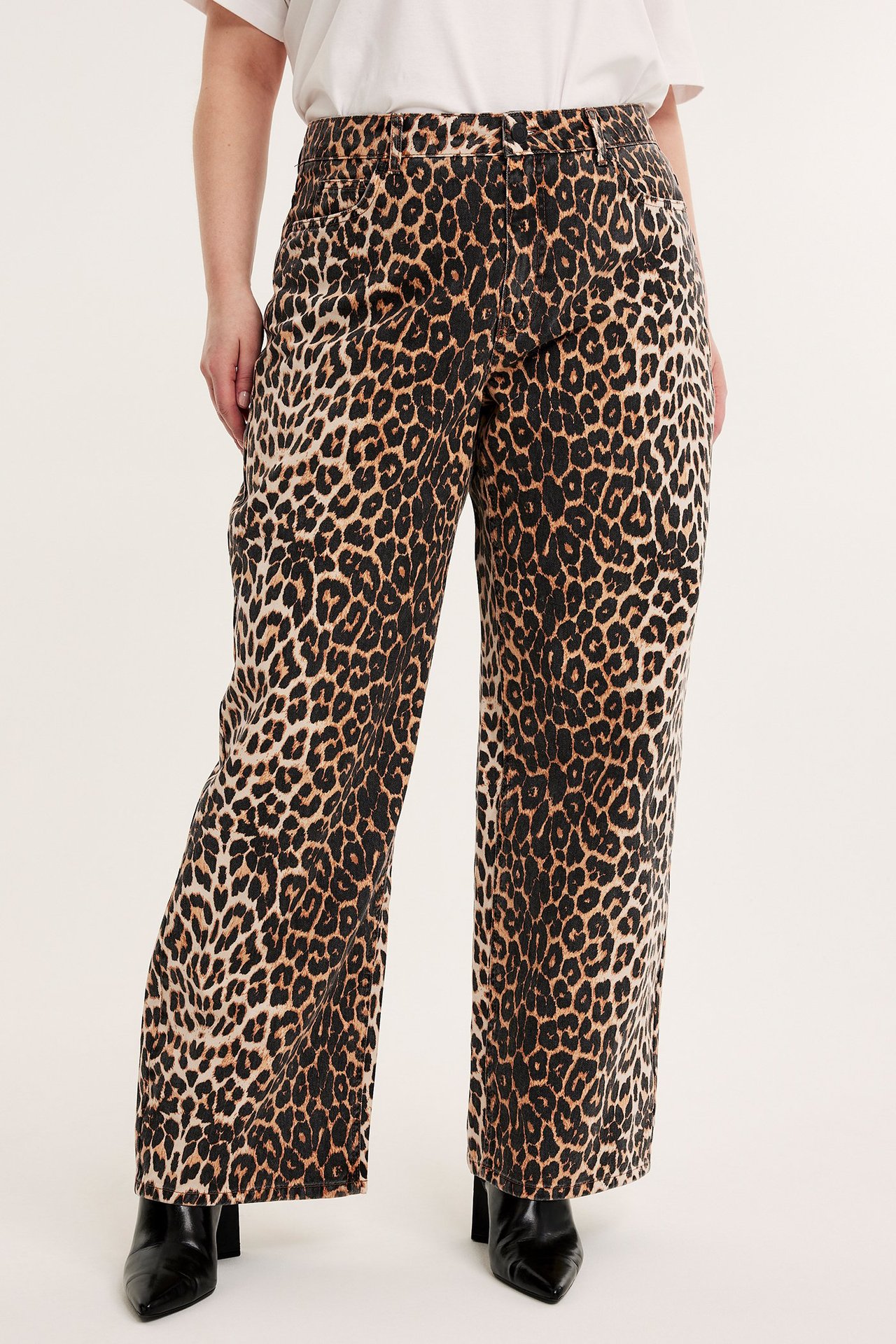 Framifrån: Kvinna i vida beiga bomullsbyxor med leopardmönster, vit t-shirt och svarta stövlar.