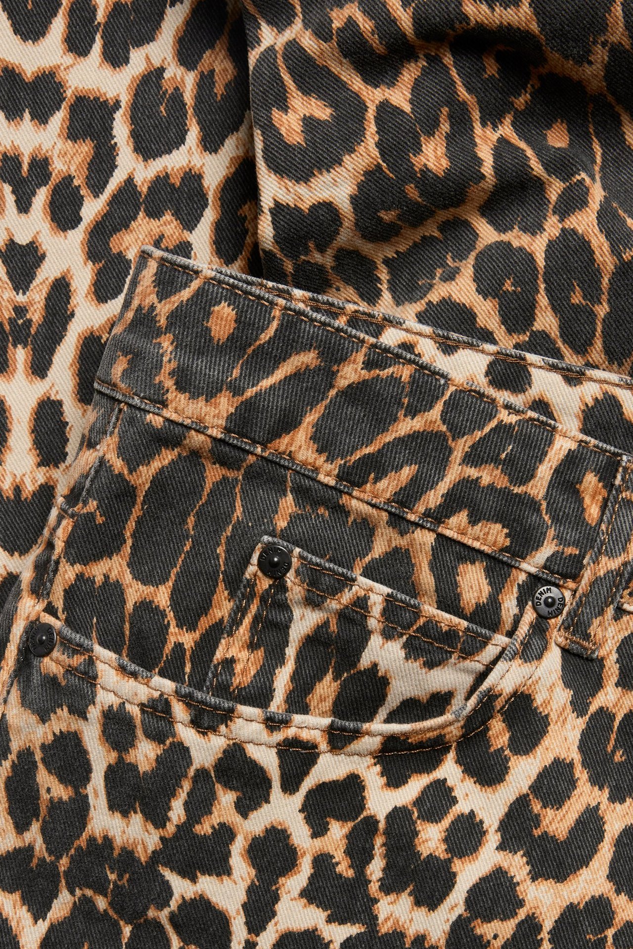 Zbliżenie beżowych bawełnianych szerokich spodni w czarno-brązowy wzór lamparta z przednią kieszenią.