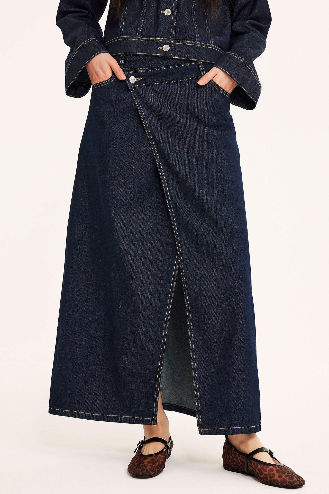 Framifrån, kvinna i lång mörk jeansomlottkjol, matchande jacka och leopardmönstrade ballerinaskor.