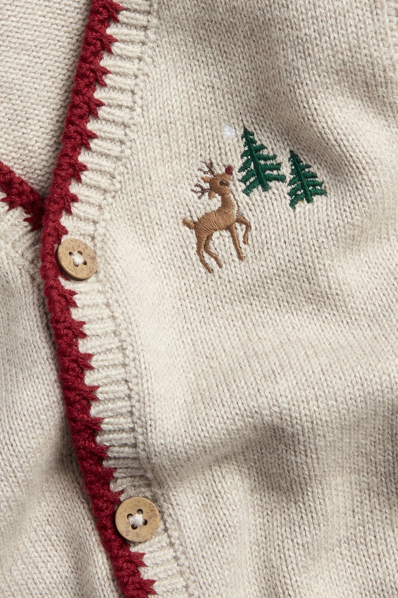 Nærbilde av en beige melert strikket bomullsvest med broderte reinsdyr, trær og treknapper.