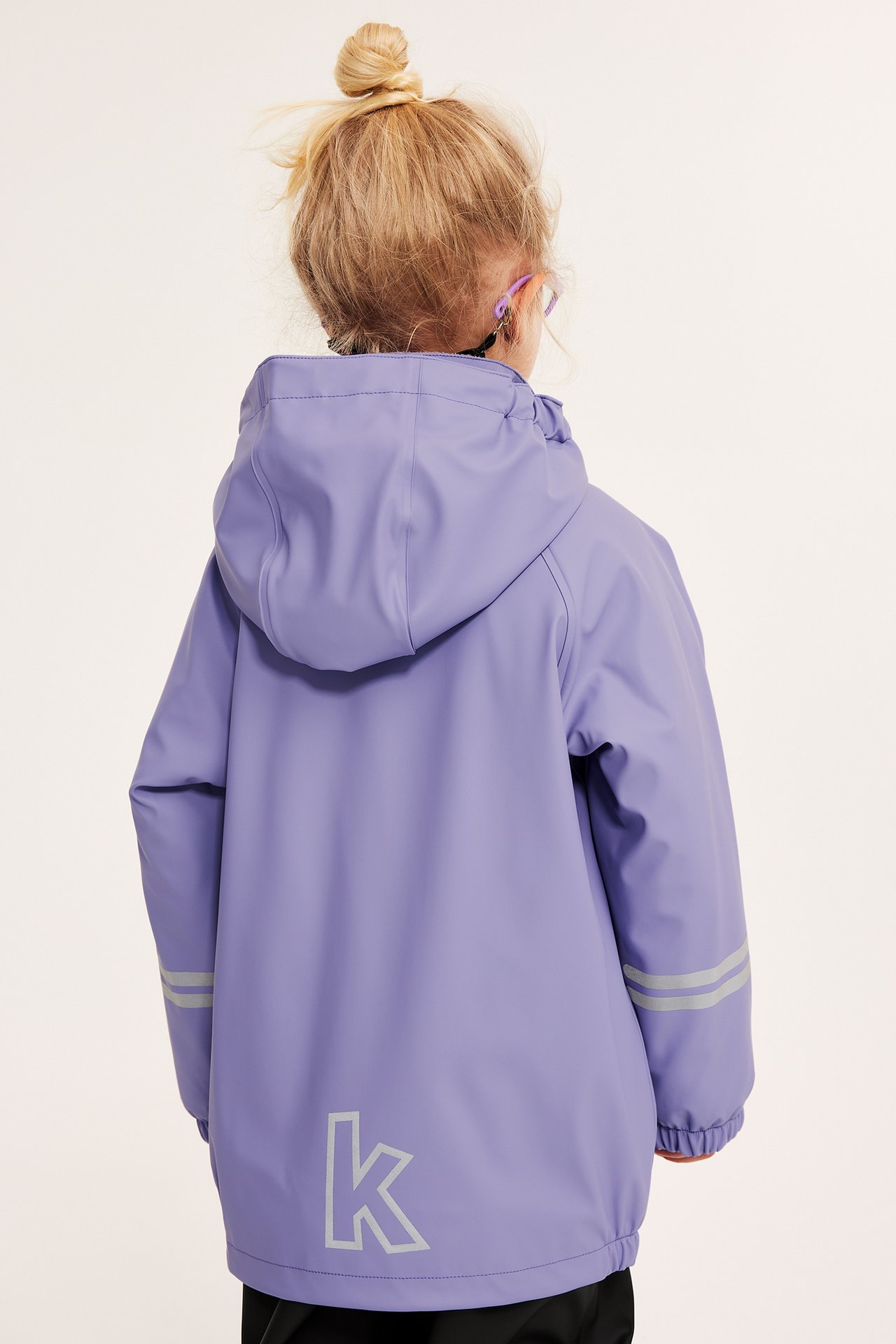 Bakfra av et barn i en lilla fleecefôret regnjakke med hette, refleksstriper og 'k'-logo.