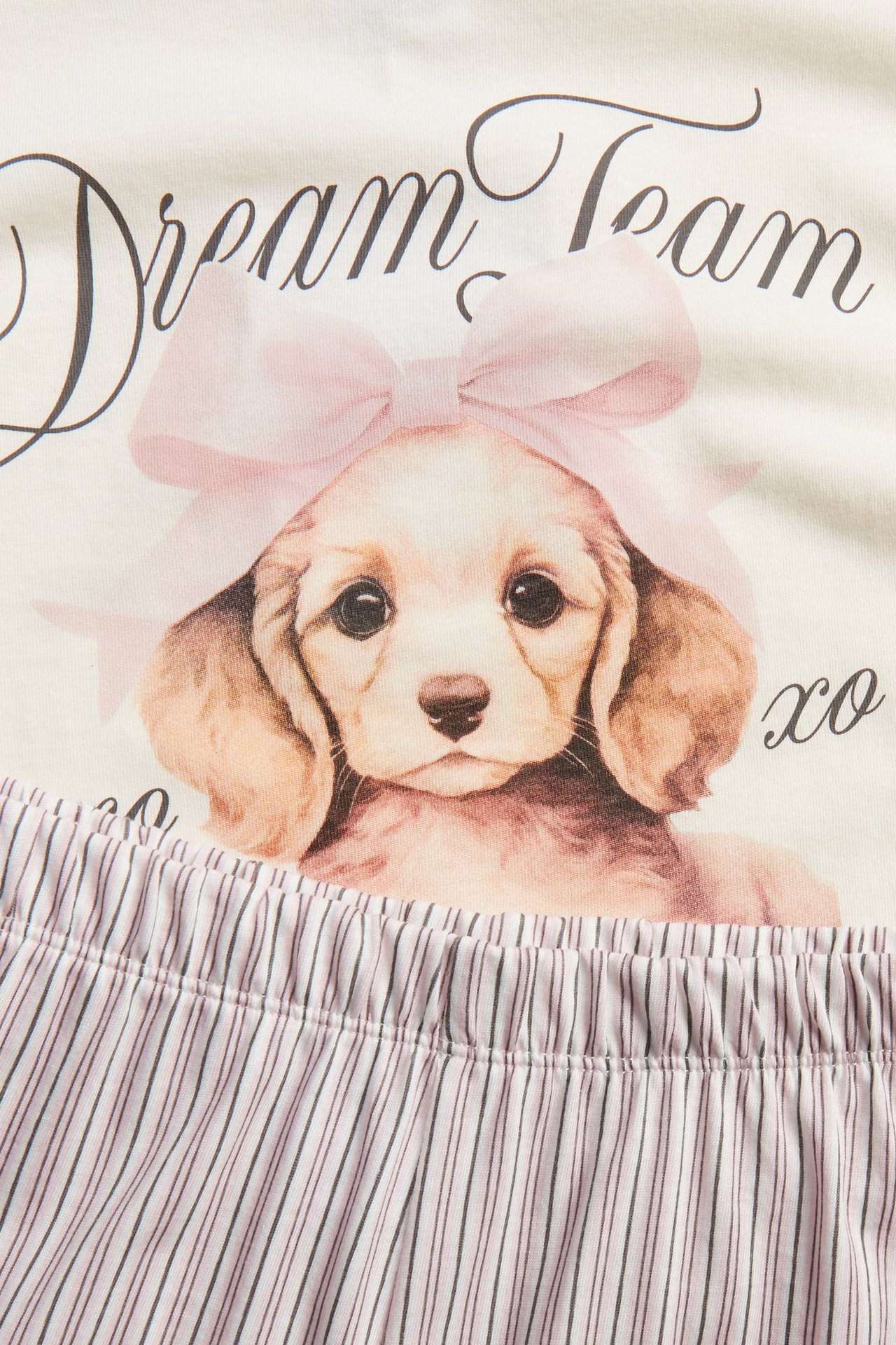 Zbliżenie na dziecięcą piżamę z off-white bawełny z nadrukiem szczeniaka i paskiem szortów w paski.