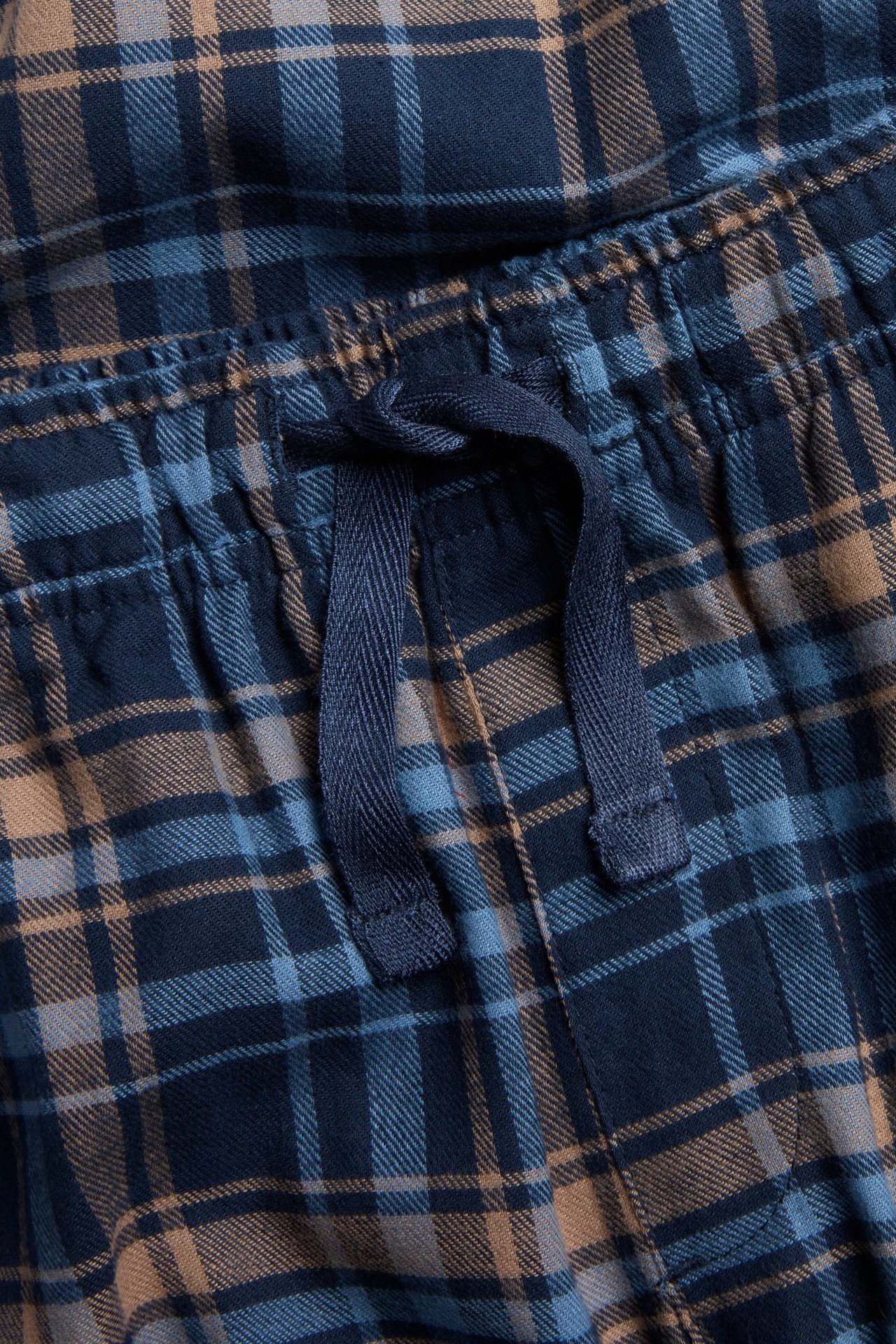 Zbliżenie na dziecięce piżamowe spodnie flanelowe w niebiesko-brązową kratę z elastyczną talią i sznurkiem.