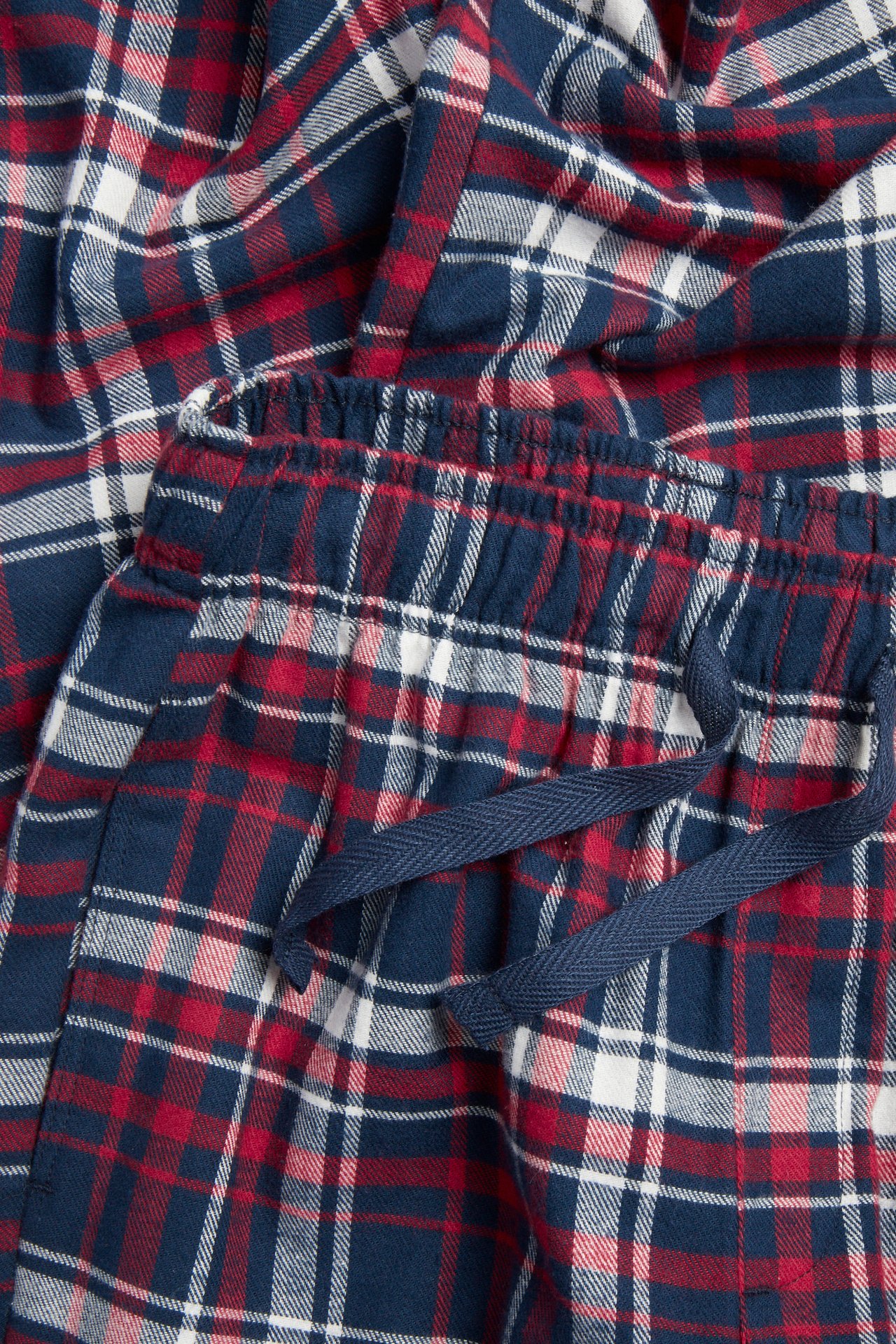 Nærbilde av røde, marineblå og hvitrutete flanellpyjamasbukser med elastisk snøring i midjen.