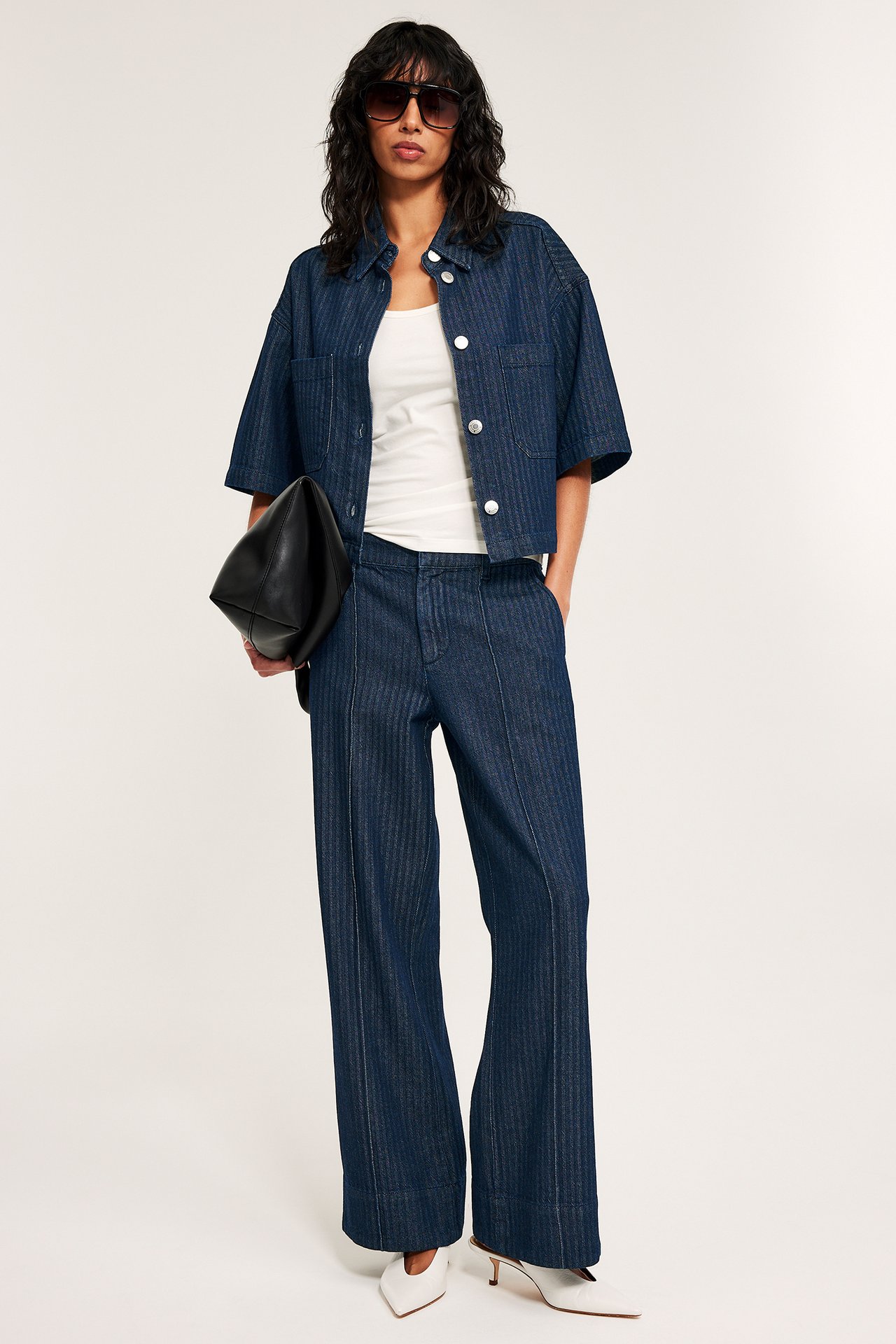 Tumman sininen lyhyt kalanruotokuviollinen farkkupaita, yhteensopivat housut, valkoinen toppi, valkoiset korot, musta laukku, aurinkolasit.