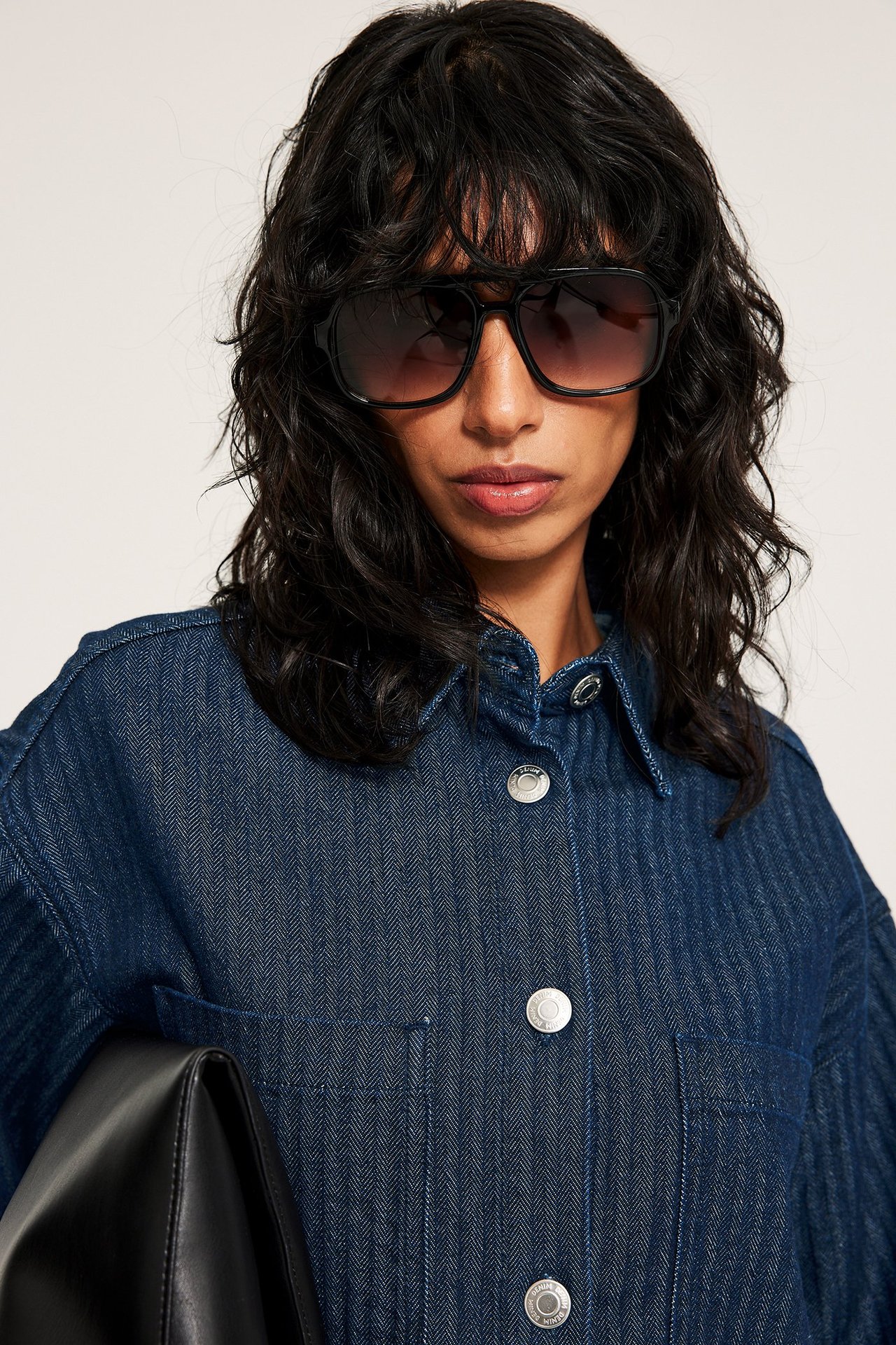 Kobieta w granatowej koszuli jeansowej w jodełkę, z napami, czarne okulary, czarna torebka.