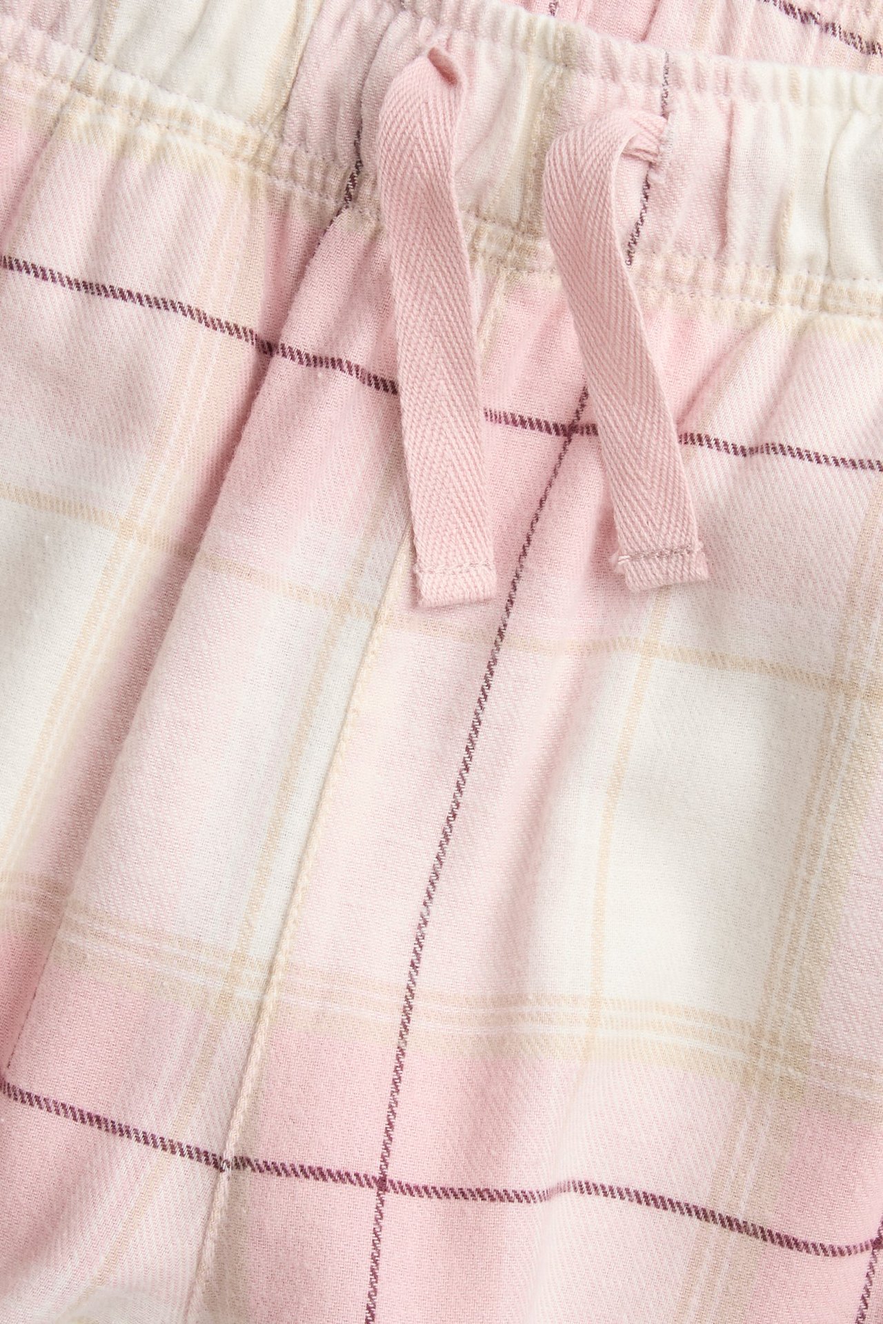 Zbliżenie na jasnoróżowe, kraciaste flanelowe spodnie piżamowe z elastycznym pasem i różowym sznurkiem.