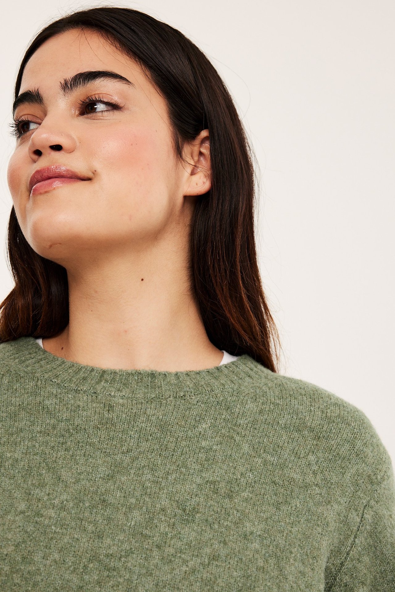 Lähikuva naisesta yllään vihreä meleerattu pyöreäkauluksinen neulepusero valkoisen aluspaidan päällä.