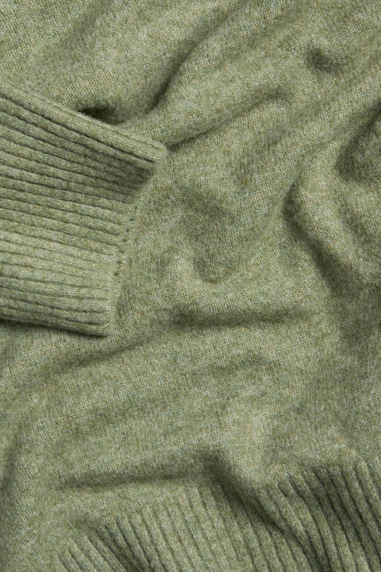 Zbliżenie zielonego melanżowego swetra z dzianiny, ze ściągaczami przy mankietach i u dołu.