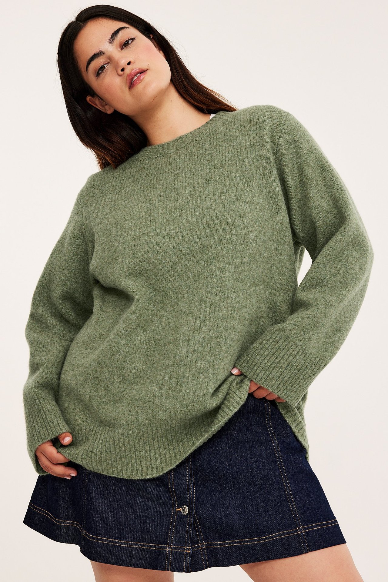 Edestä: nainen yllään meleerattu vihreä pyöreäkauluksinen neulepusero ja tummansininen farkkuhame.