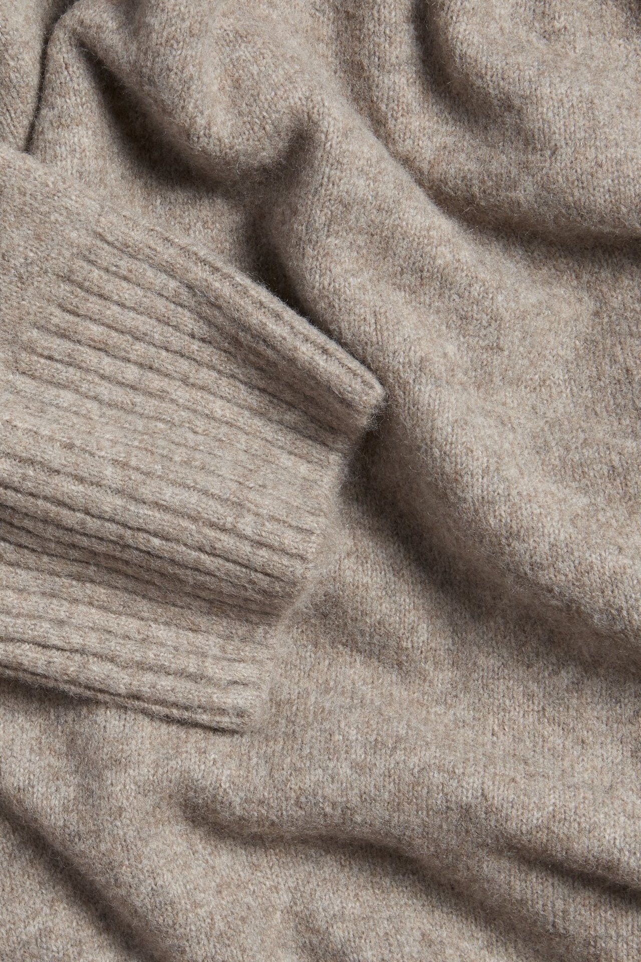 Zbliżenie beżowego melanżowego swetra dzianinowego z prążkowanym mankietem.