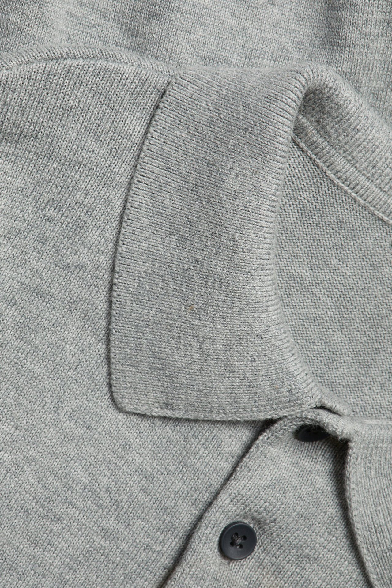 Zbliżenie na drobno dzianą, ciemnoszarą bawełnianą koszulkę polo z kołnierzykiem i ciemnymi guzikami.