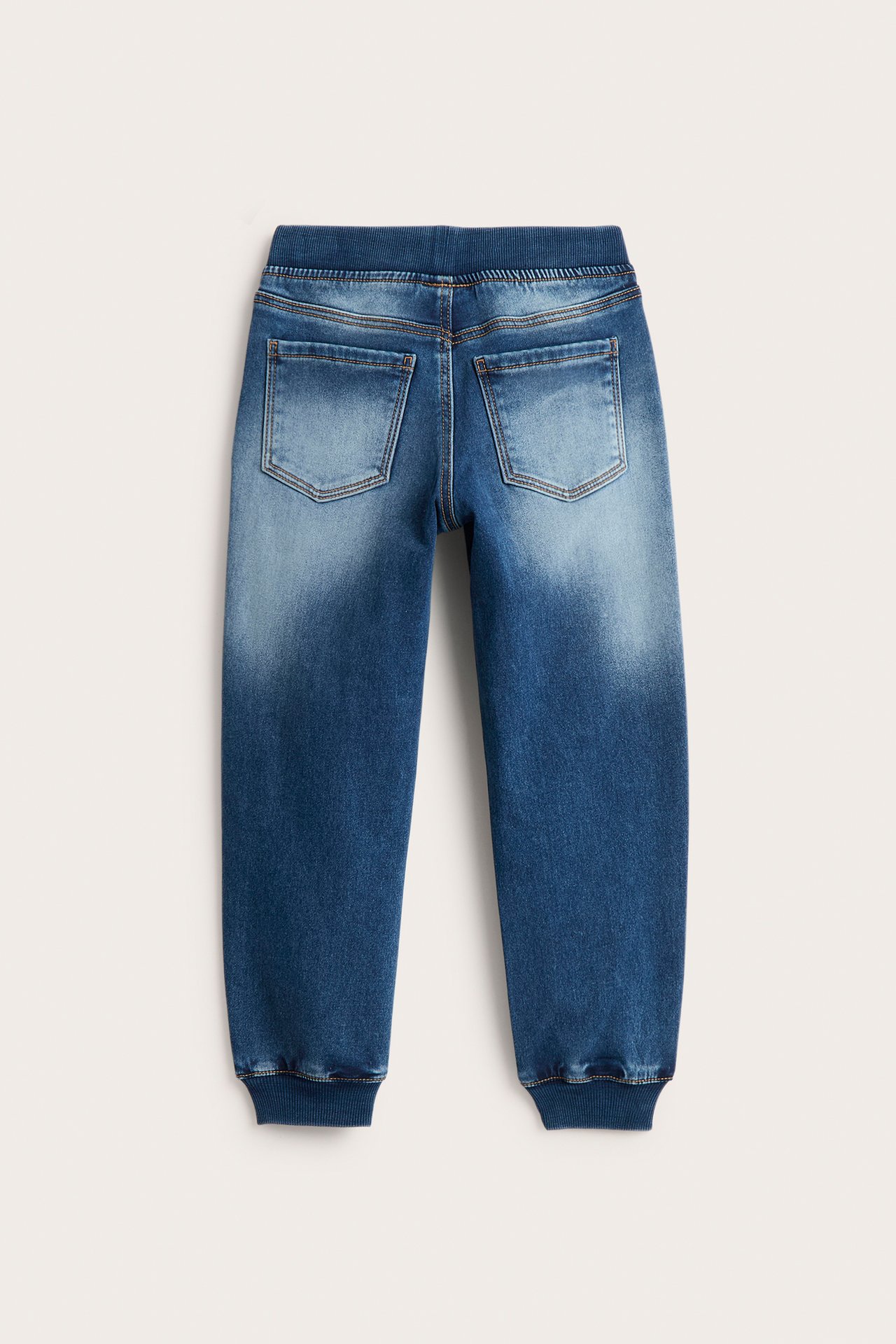 Bakifrån: barnjeans i blekt blå joggerdenim med ribbad midja, muddar och två bakfickor.