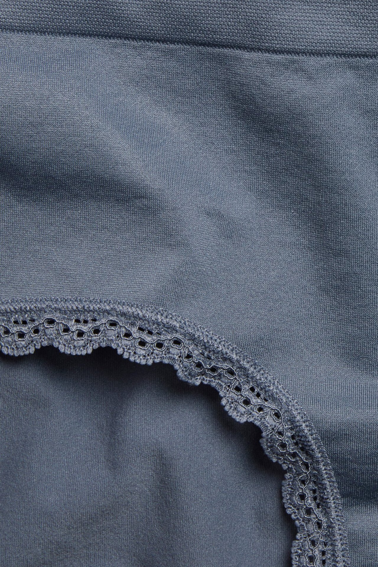 Zbliżenie na ciemnoniebieskie bezszwowe figi typu hipster z delikatną koronkową lamówką.