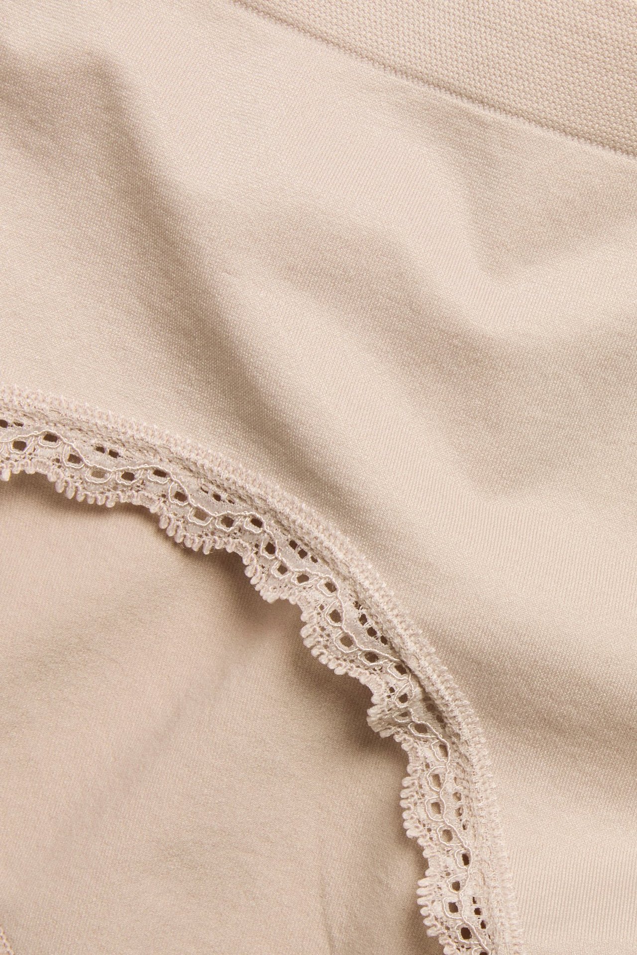 Zbliżenie na jasnoróżowe, bezszwowe figi typu hipster z delikatną koronkową krawędzią.