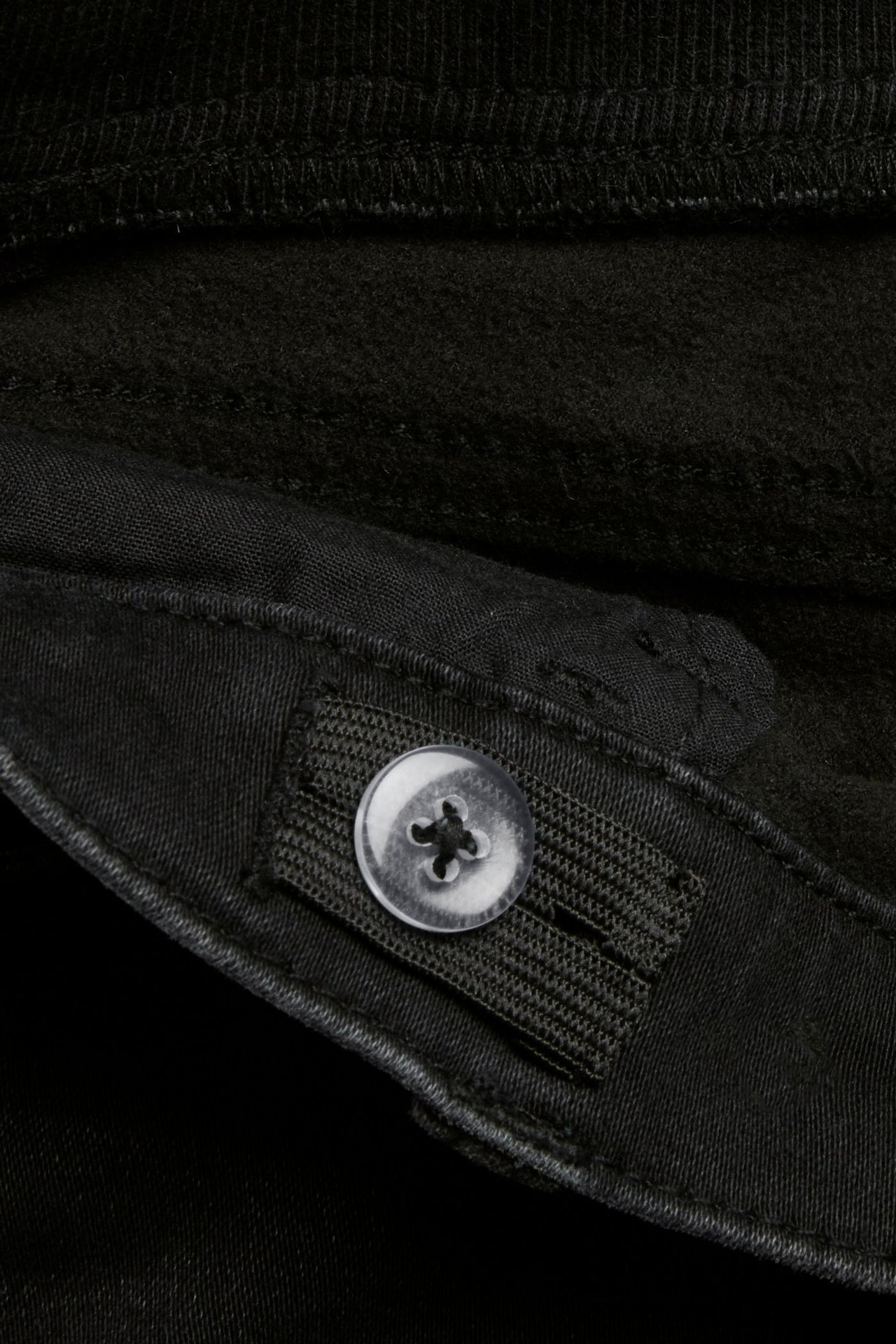 Zbliżenie na czarne dżinsy jogger denim dla dzieci, pokazujące regulowany pas z gumką i przezroczystym guzikiem.