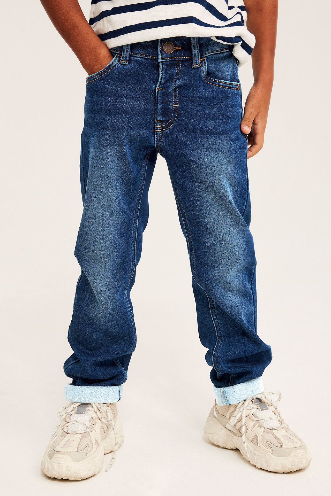 Forfra: Barn i blå straight jogger jeans med oppbrettede benkanter, stripete t-skjorte og lysbeige sneakers.