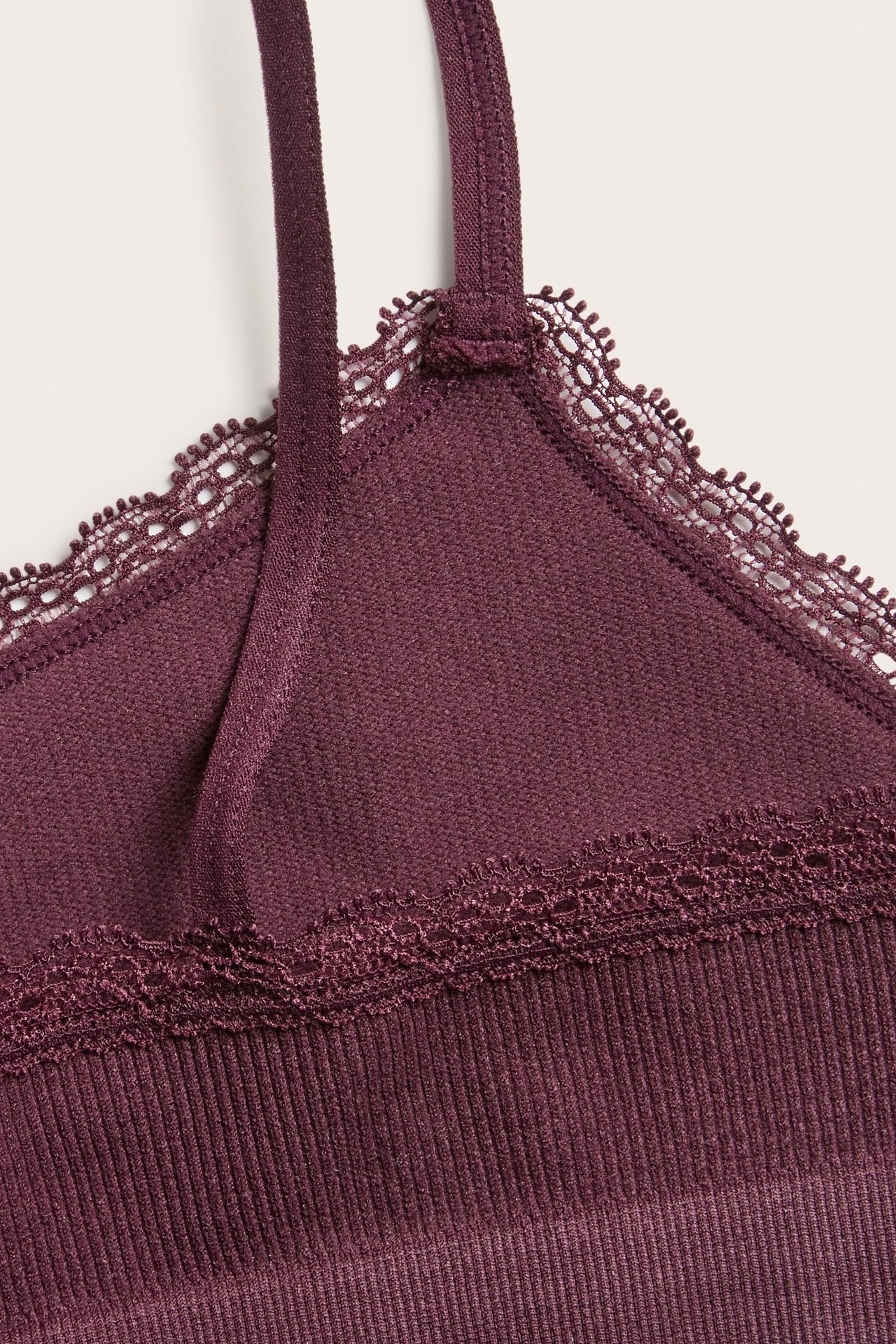 Zbliżenie na bordowy, bezszwowy, prążkowany top z koronkową lamówką wzdłuż dekoltu i ramiączek.