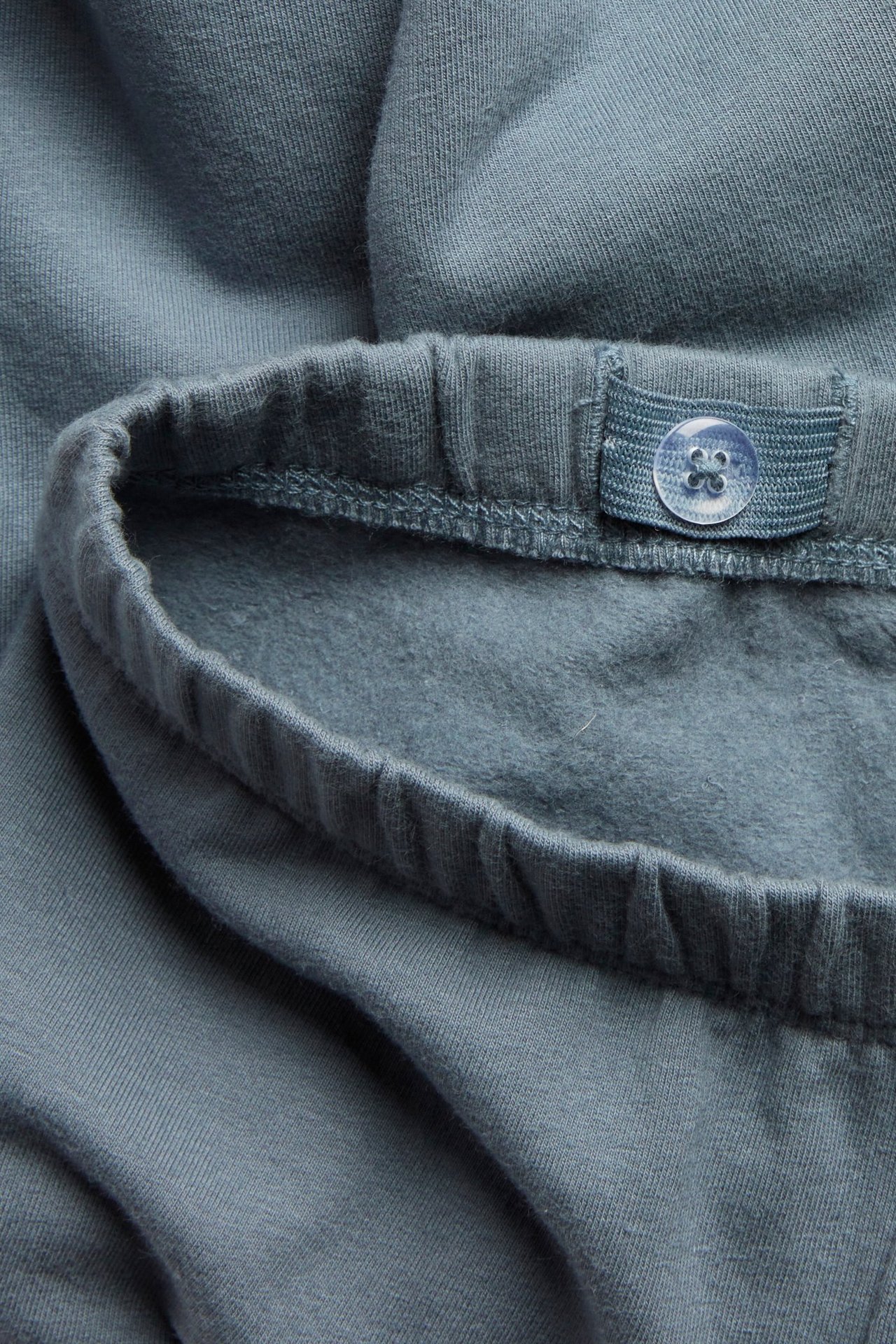 Zbliżenie niebieskich legginsów z elastycznym pasem i regulowanym guzikiem, widoczna szczotkowana strona wewnętrzna.