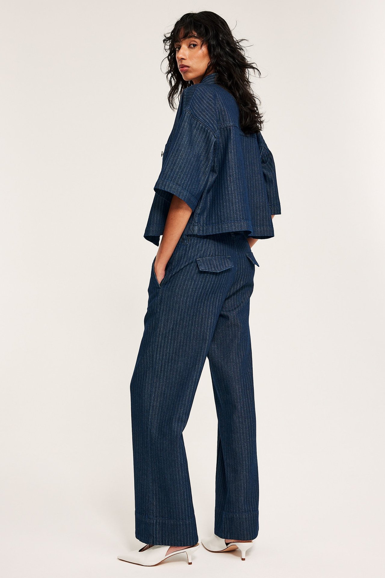 Sidebilde: kvinne i mørkeblå fiskebensmønstrede vide jeans, matchende skjorte og hvite mules.