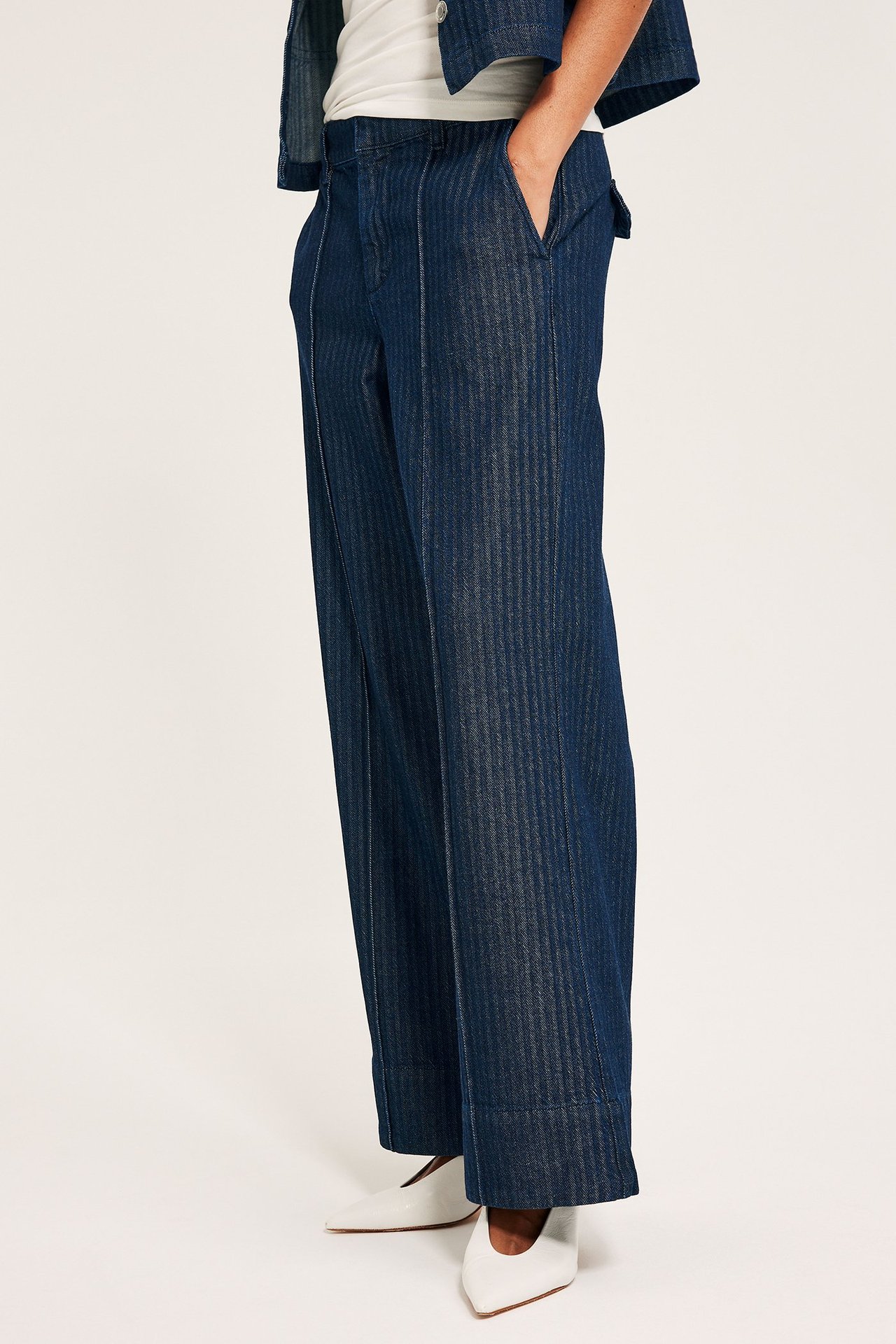 Sidovy av kvinna i mörkblå vida högmidjade jeans, vit topp och vita skor.