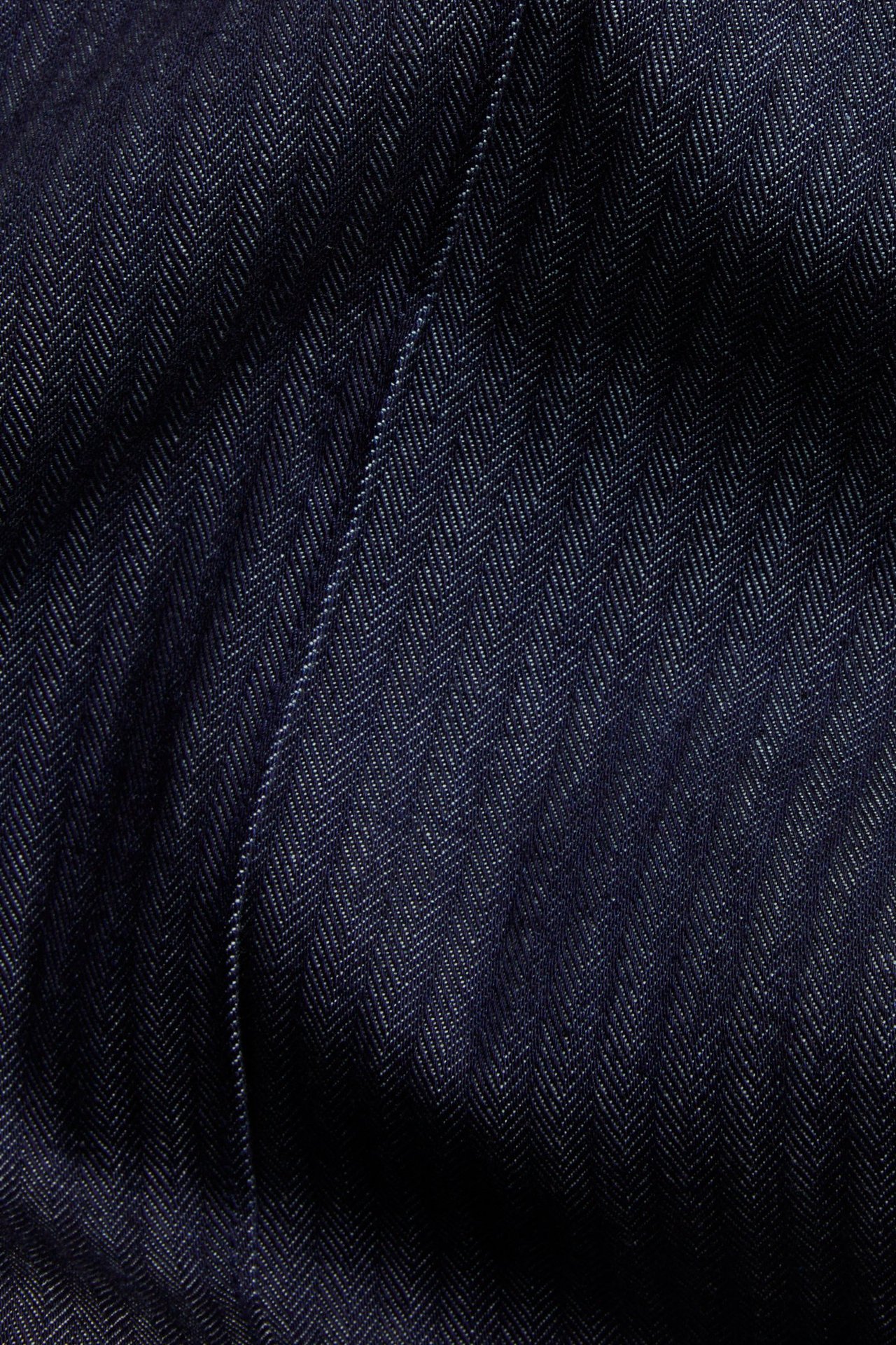 Zbliżenie na ciemny dżinsowy materiał w jodełkę z widocznym szwem.