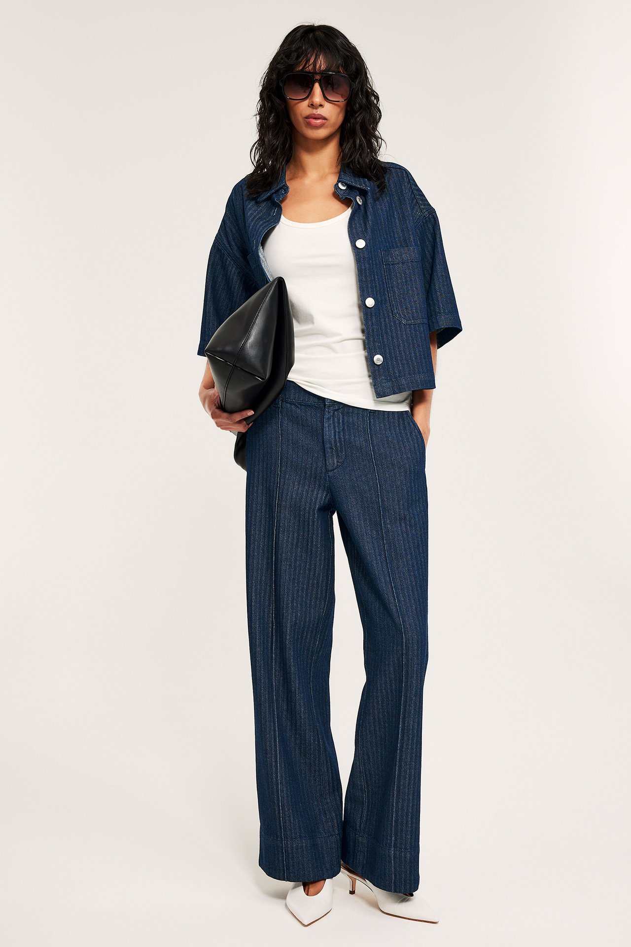 Mørkeblå jacquard-vevde vide jeans med høyt liv, matchende kort skjorte og hvit singlet på en kvinne.