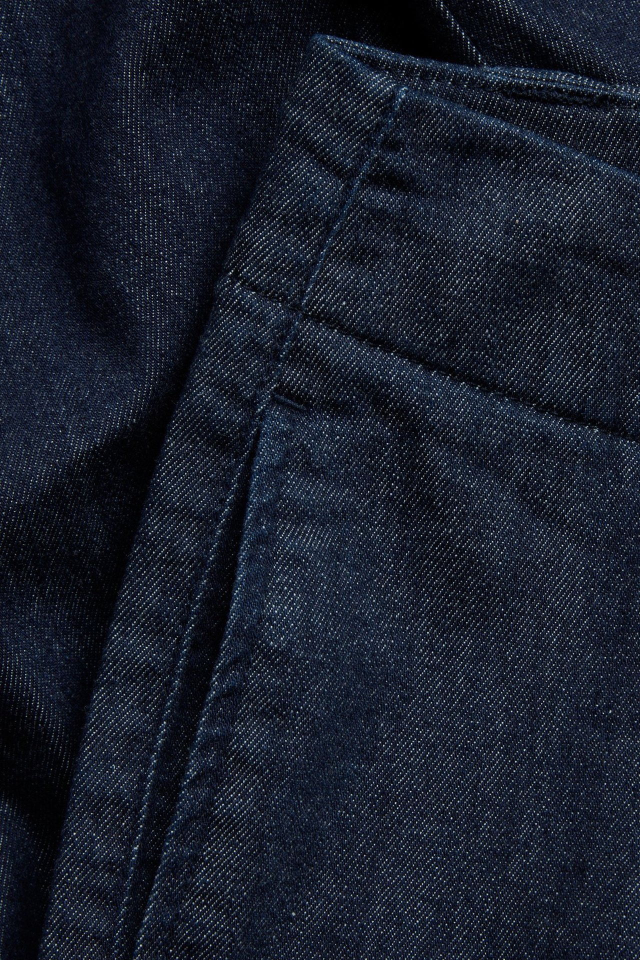 Zbliżenie na ciemne dżinsy cropped z prostymi nogawkami, ukazujące fakturę materiału i kieszeń boczną.