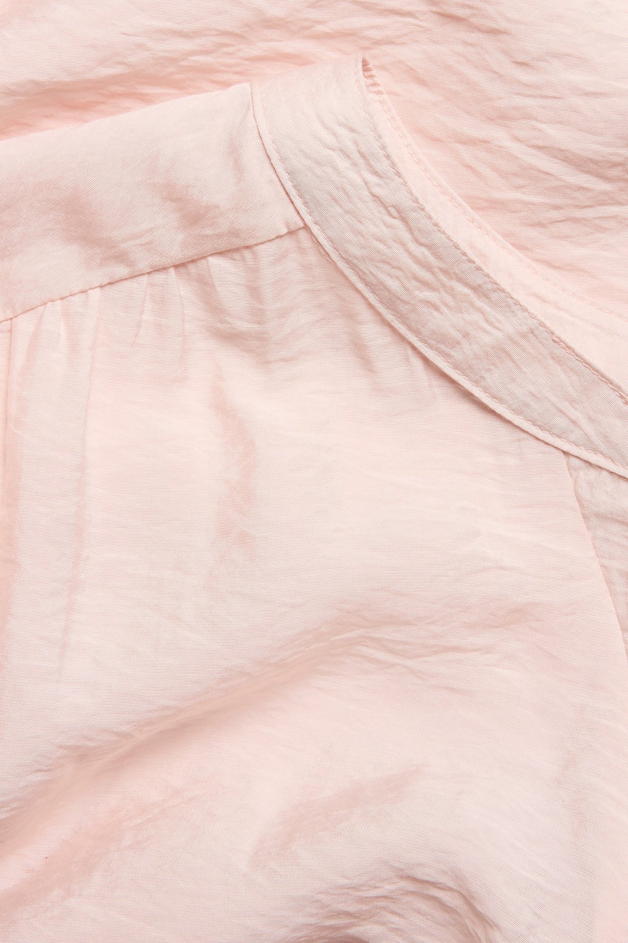 Zbliżenie jasnobeżowej, teksturowanej bluzki z detalem kołnierza.