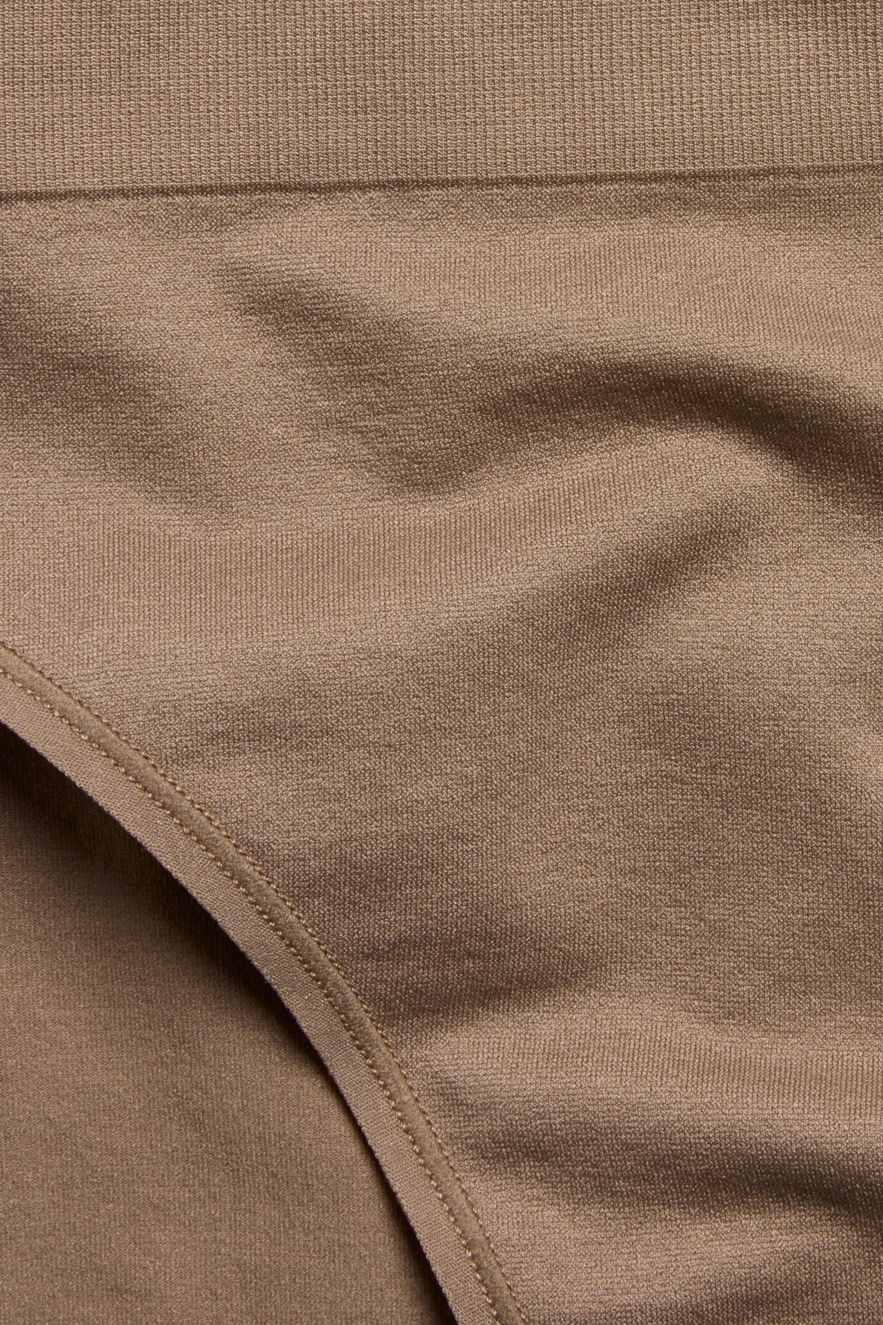 Zbliżenie beżowych, jednolitych majtek z miękkiej tkaniny poliamidowo-elastanowej z prążkowanym pasem.