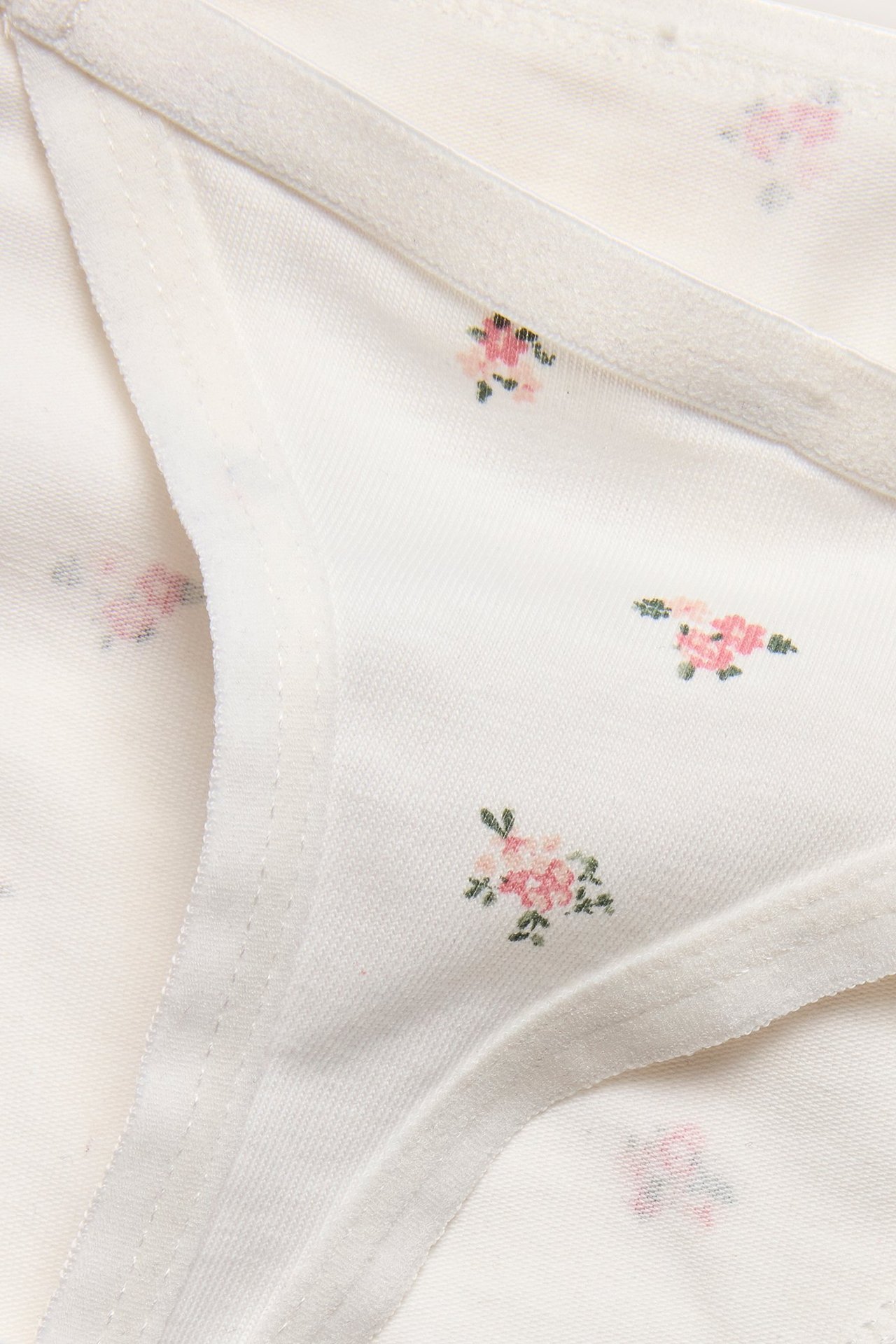 Närbild av offwhite stringtrosor i bomullsblandning med små rosa blommor och smal resår.