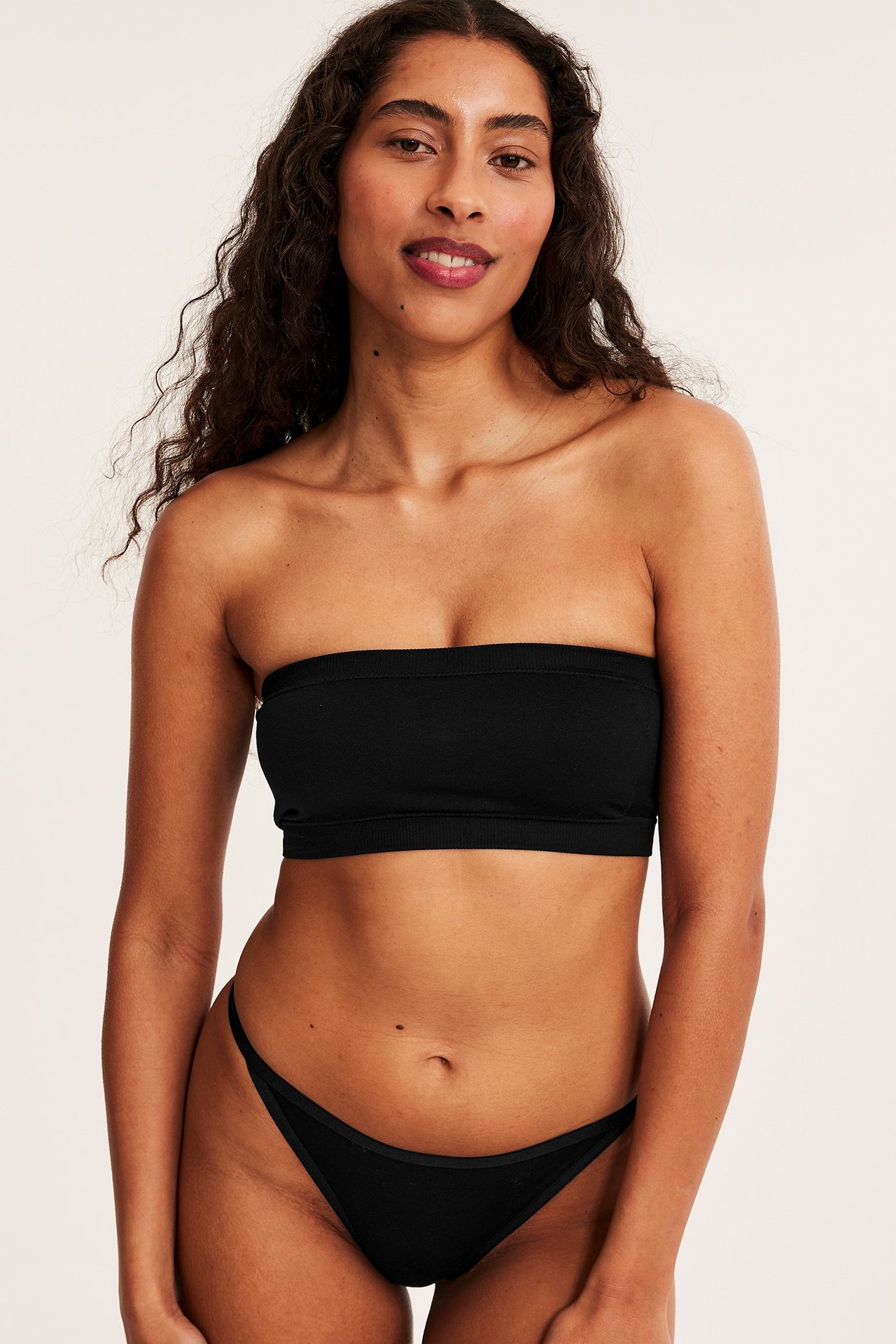 Framifrån, kvinna i svarta bomullsstringtrosor med smal resår och en svart bandeau-topp.