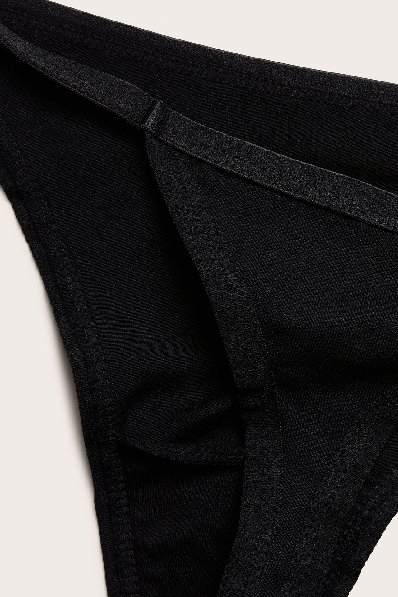 Zbliżenie na czarne, jednolite stringi z mieszanki bawełny z wąską gumką.