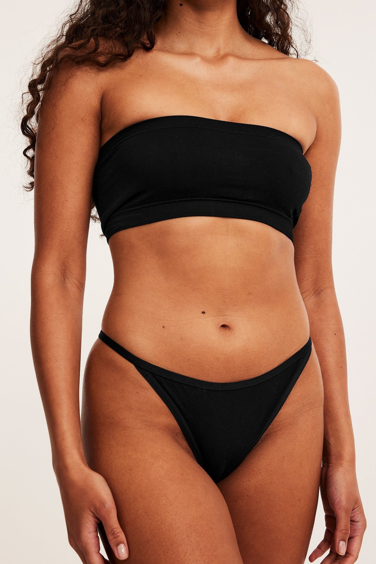 Frontbilde av en kvinne i svart bomullsstringtruse med smal strikk og en svart bandeau-topp.