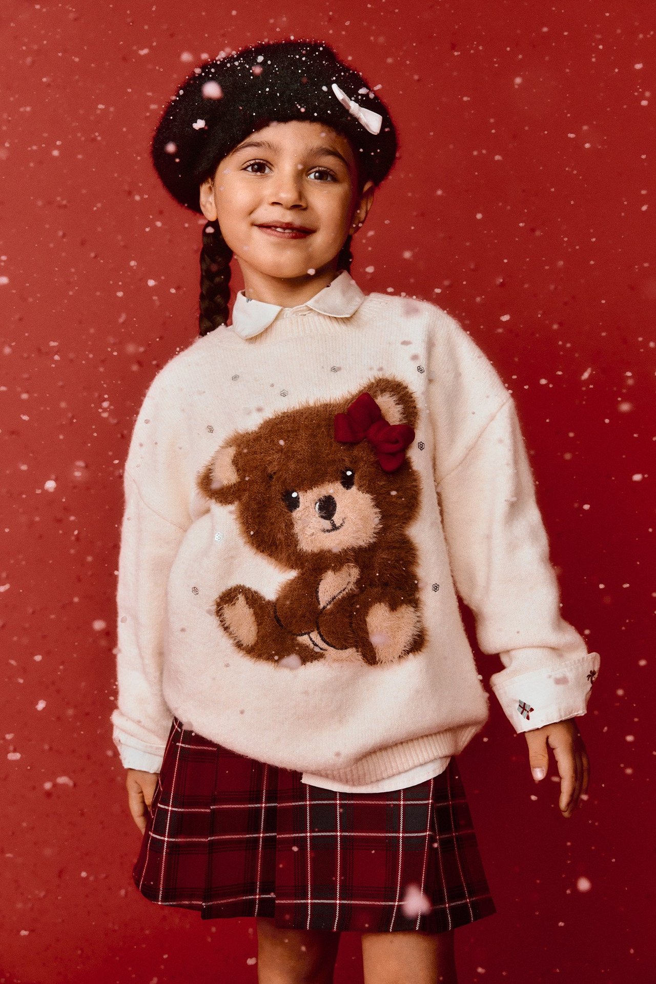Forfra: Barn i offwhite teddybjørn-strikkegenser med paljetter, hvit skjorte, rødrutete skjørt, svart beret.