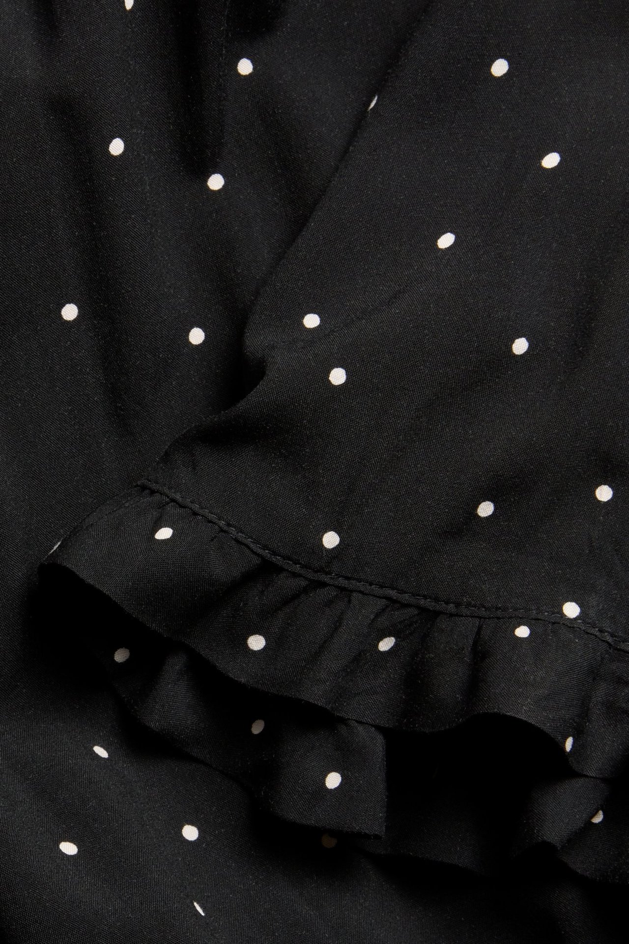 Zbliżenie czarnej sukienki midi w białe kropki z falbankowym krótkim rękawem.